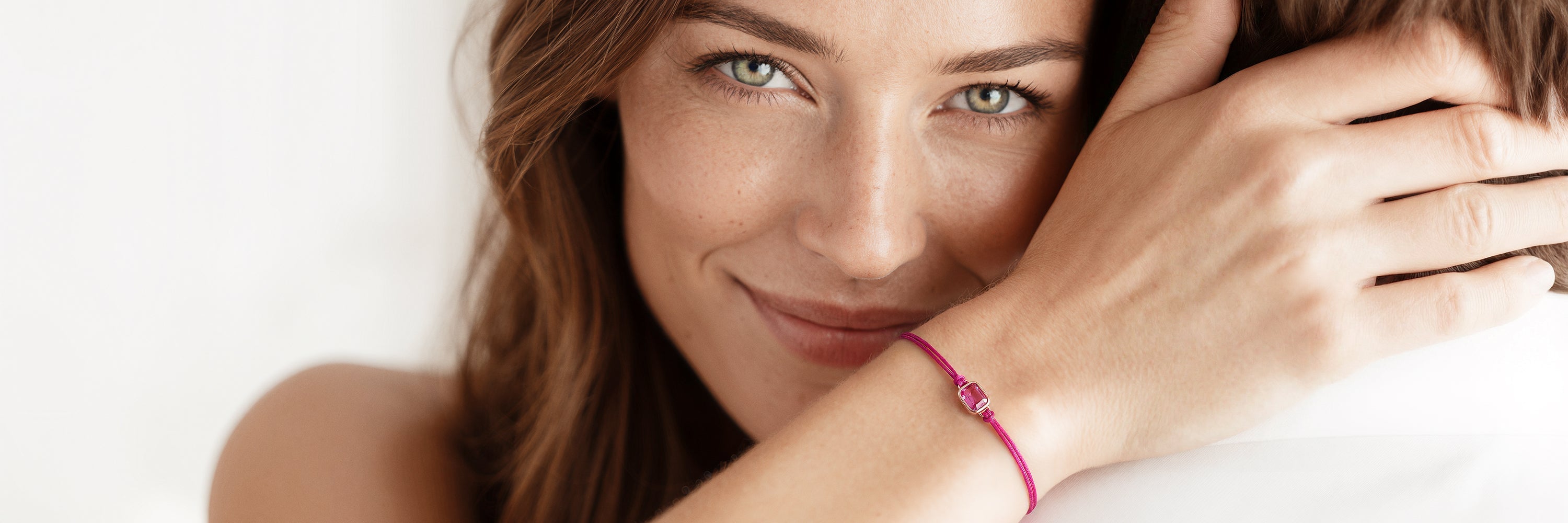 Ein zartes goldenes Armband mit einem kleinen Verschluss steht zentriert vor einem sanften grauen Hintergrund. Das Wort „LOVE“ ist in großen rosa Buchstaben deutlich hinter dem Armband zu sehen.