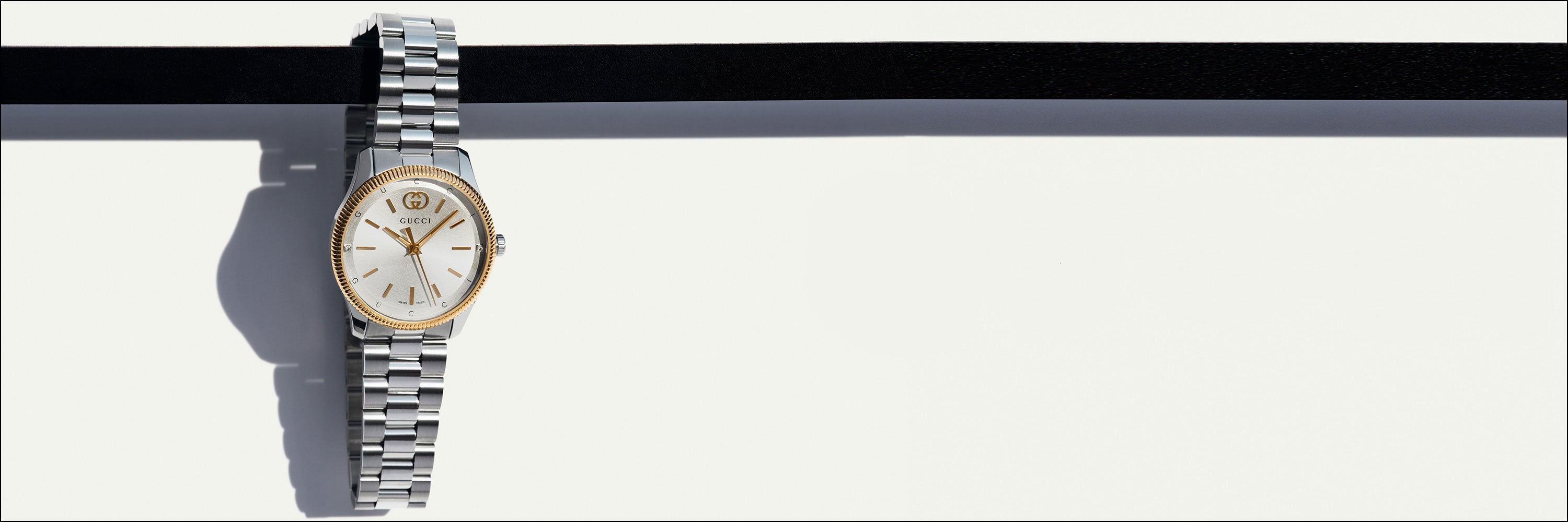 Eine elegante silberne Gucci-Armbanduhr mit schwarzem Zifferblatt und Metallarmband auf weißem Hintergrund. Auf der rechten Seite sind das Gucci-Logo und das Wort „Uhren“ abgebildet.