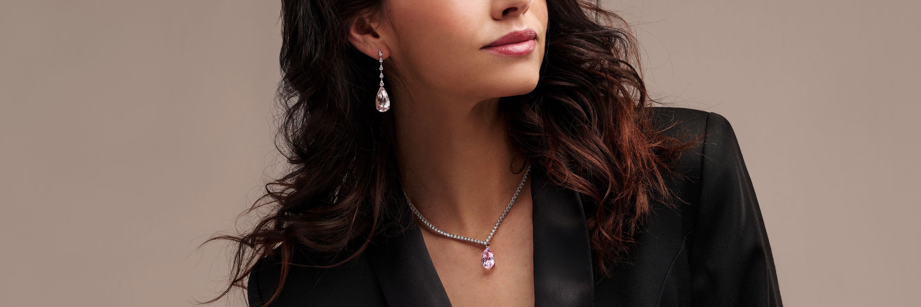 Hinter einer weißen Blende ist teilweise eine Person in einem weißen Langarmhemd zu sehen. An ihren Fingern trägt sie einen Ring mit blauem Stein. In der Hand hält sie eine schwarze Schmuckschatulle mit einem weiteren Ring mit blauen Steinen darin.