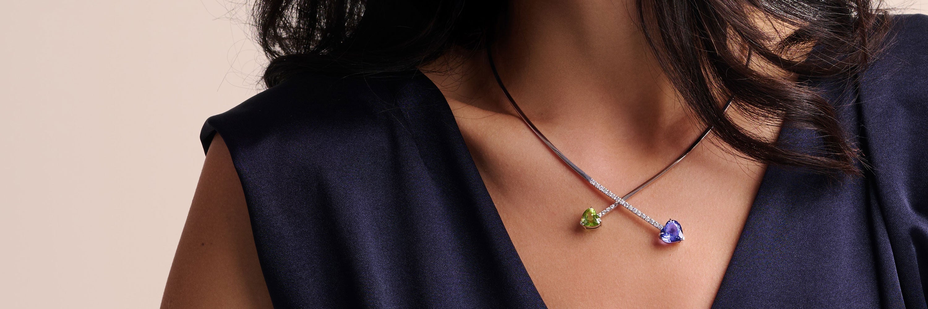 Eine Frau, teilweise verdeckt durch ein weißes Laken, trägt ein schwarzes Kleid mit V-Ausschnitt und eine mehrreihige grüne Halskette. Das Bild ist minimalistisch mit einem weichen, neutralen Hintergrund.