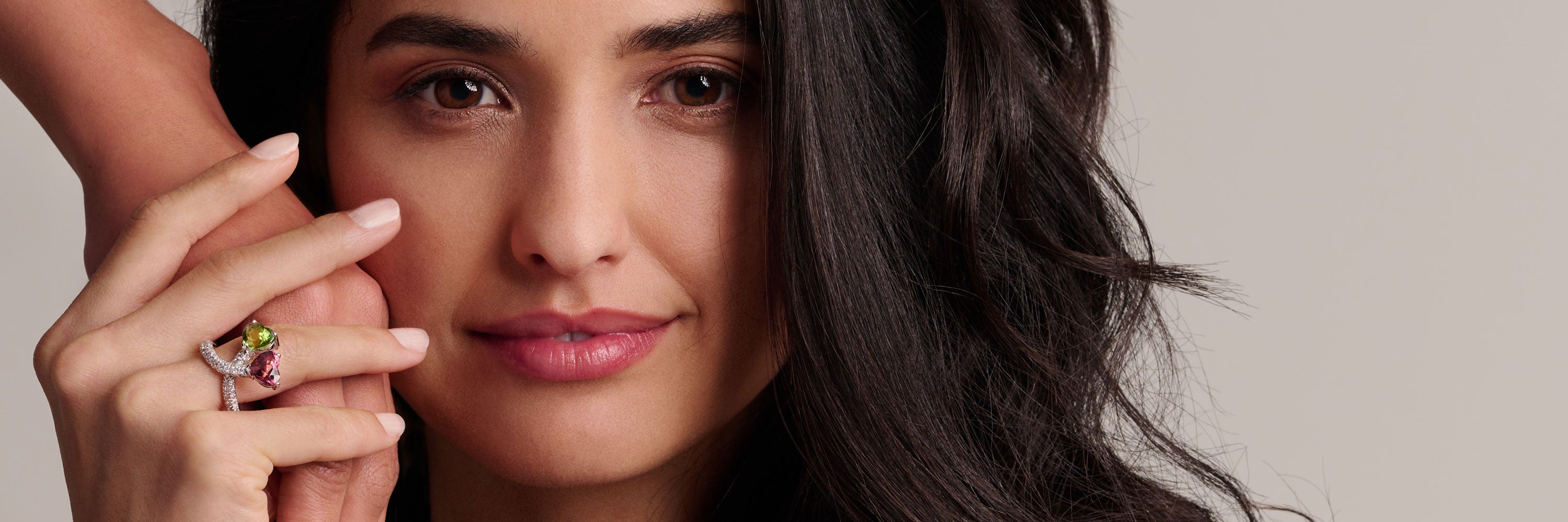 Ein mit Edelstein besetzter Ring ziert den Zeigefinger einer Dame. Es wird nur die Hand gezeigt, der Hintergrund ist in einem neutralen Farbton gehalten.