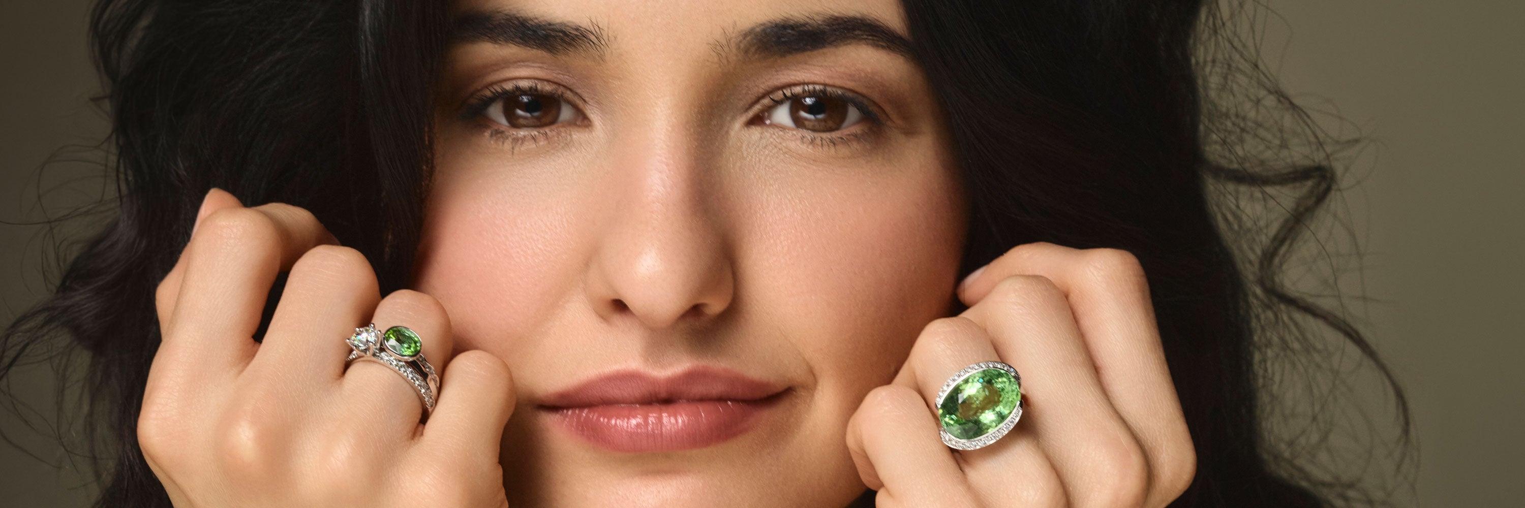 Ein mit Edelstein besetzter Ring ziert den Zeigefinger einer Dame. Es wird nur die Hand gezeigt, der Hintergrund ist in einem neutralen Farbton gehalten.