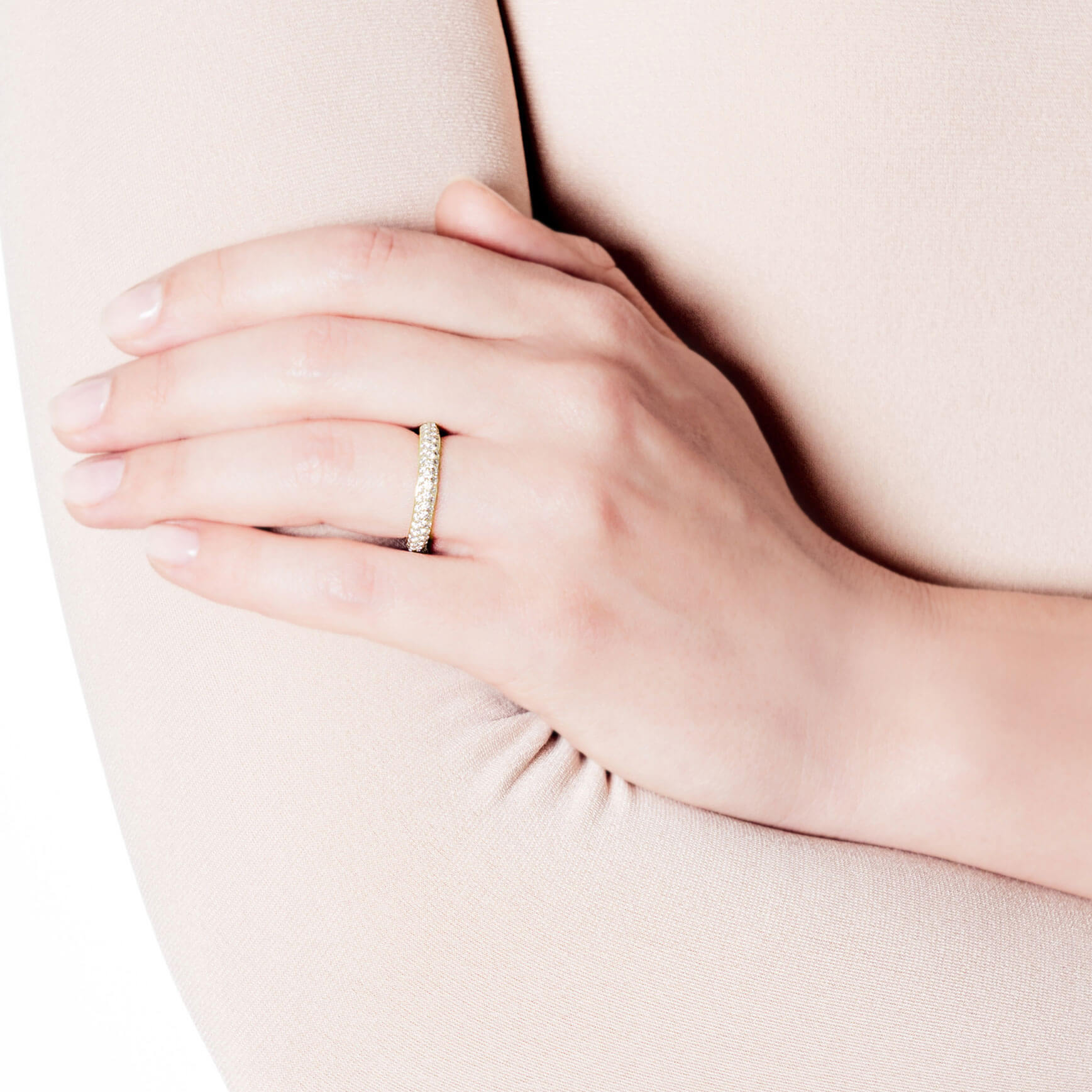 Eine Person hält sanft ihren Arm und präsentiert einen atemberaubenden Schullin Memoire-Ring in Gelbgold, der mit kleinen Diamanten an ihrem Ringfinger verziert ist. Der neutrale Hintergrund unterstreicht die Eleganz des Schmucks.
