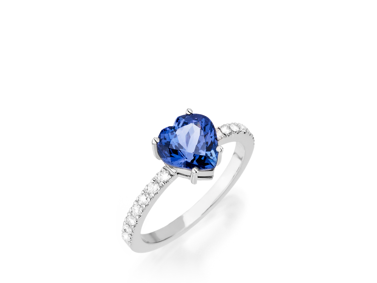 Wir präsentieren den TANSANIT RING HEART von Schullin: Ein Weißgoldring mit einem herzförmigen Tansanit-Edelstein in der Mitte, der entlang der Ringschiene wunderschön mit kleinen runden Diamanten verziert ist.