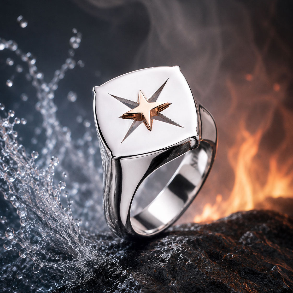 Der ELEMENTS RING SILBER von Schullin zeigt ein goldenes Sternmotiv auf Silber, das auf einem dunklen Felsen mit Wasserspritzern und Flammen im Hintergrund die elementaren Kräfte von Wasser und Feuer repräsentiert.