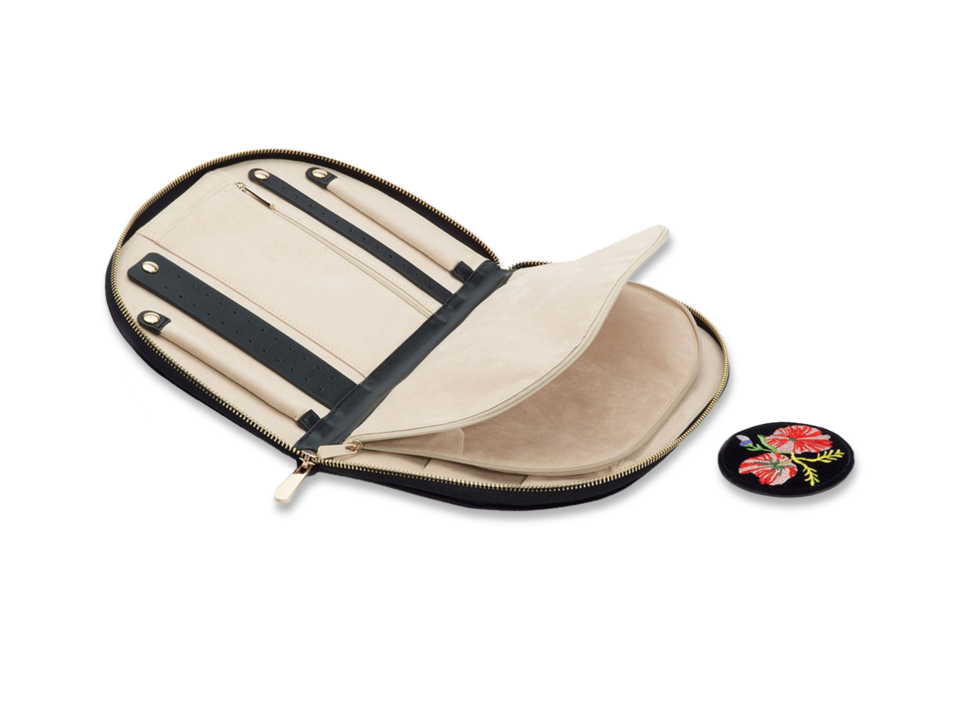 Die SCHMUCKTASCHE von Schullin, eine beigefarbene Schmuckschatulle mit Reißverschluss, lässt sich öffnen und gibt den Blick auf Fächer und Riemen frei. Daneben liegt ein runder schwarzer Aufnäher, der mit gestickten roten und weißen Blumen und grünen Blättern verziert ist.