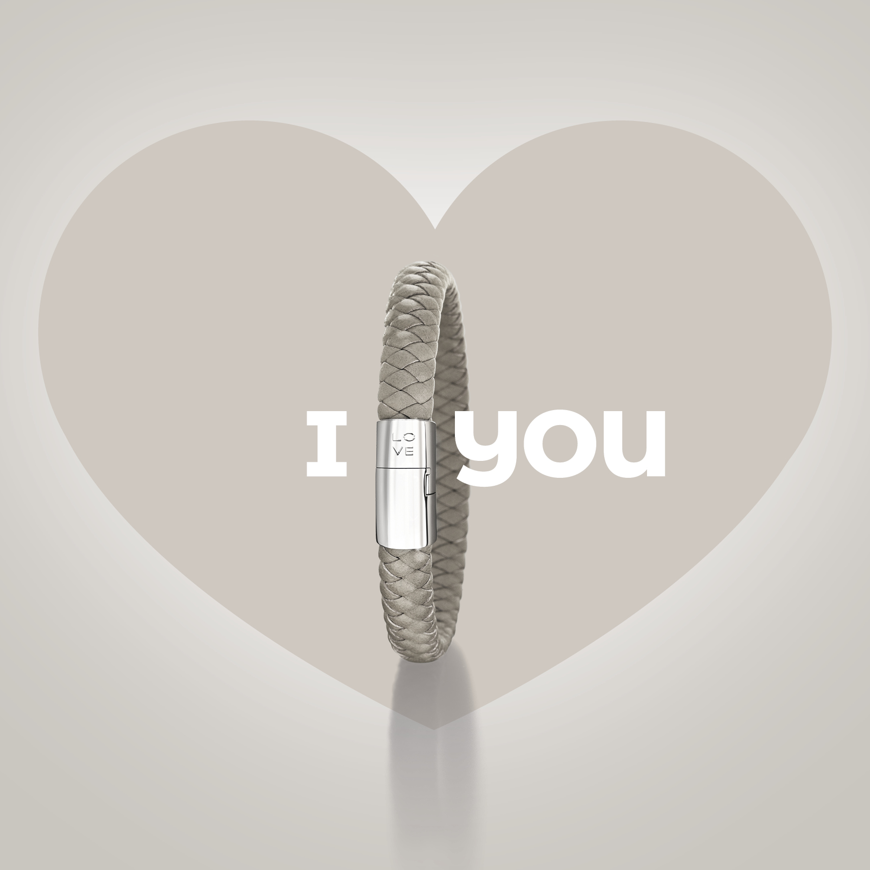 Das Schullin POWER ARMBAND aus Leder in Beige, mit Sterling-Silber-Schließe graviert mit "LOVE", bildet das "O" in "I love you" vor hellem Hintergrund mit großem Herz.
