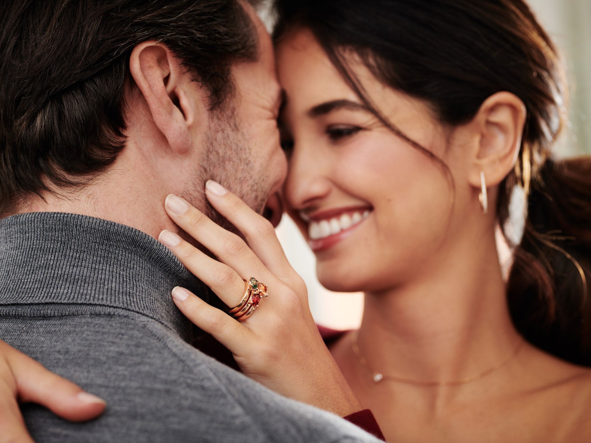 Eine Frau lächelt und umarmt einen Mann, wobei sie den Schullin TURMALIN RING FANCY T an ihrer Hand vorzeigt. Sie wirken glücklich und zärtlich, ihre Gesichter berühren sich, die Augen sind geschlossen.