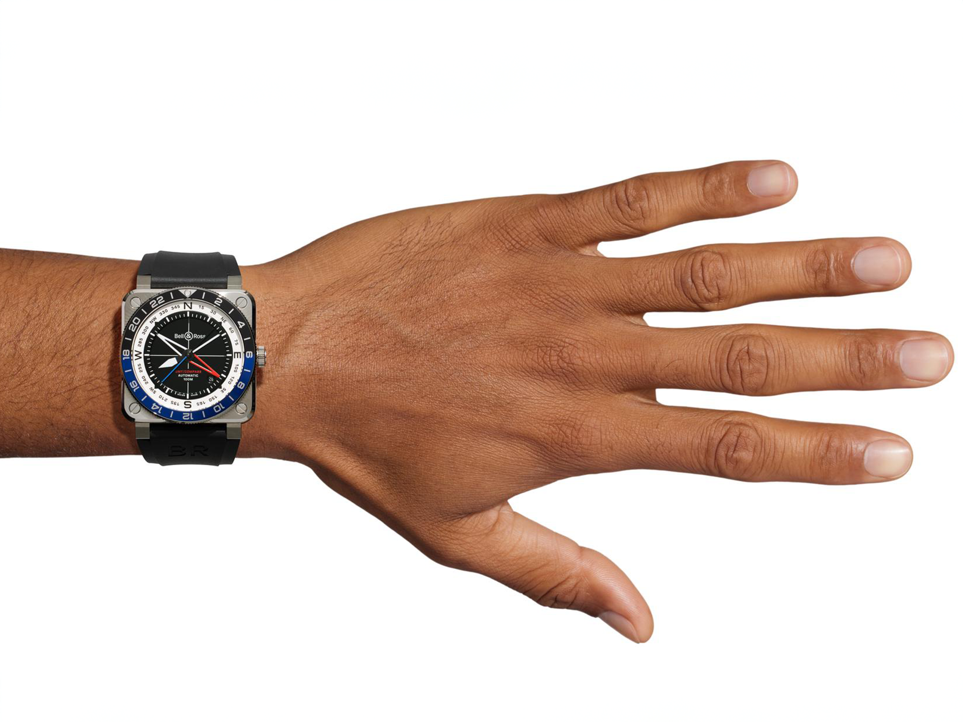Nahaufnahme einer ausgestreckten Hand, die die Schullin BELL & ROSS BR-03 GMT COMPASS trägt. Sie hat ein großes schwarz-silbernes Gehäuse, ein rundes mehrfarbiges Zifferblatt und ein schwarzes Band auf weißem Hintergrund.