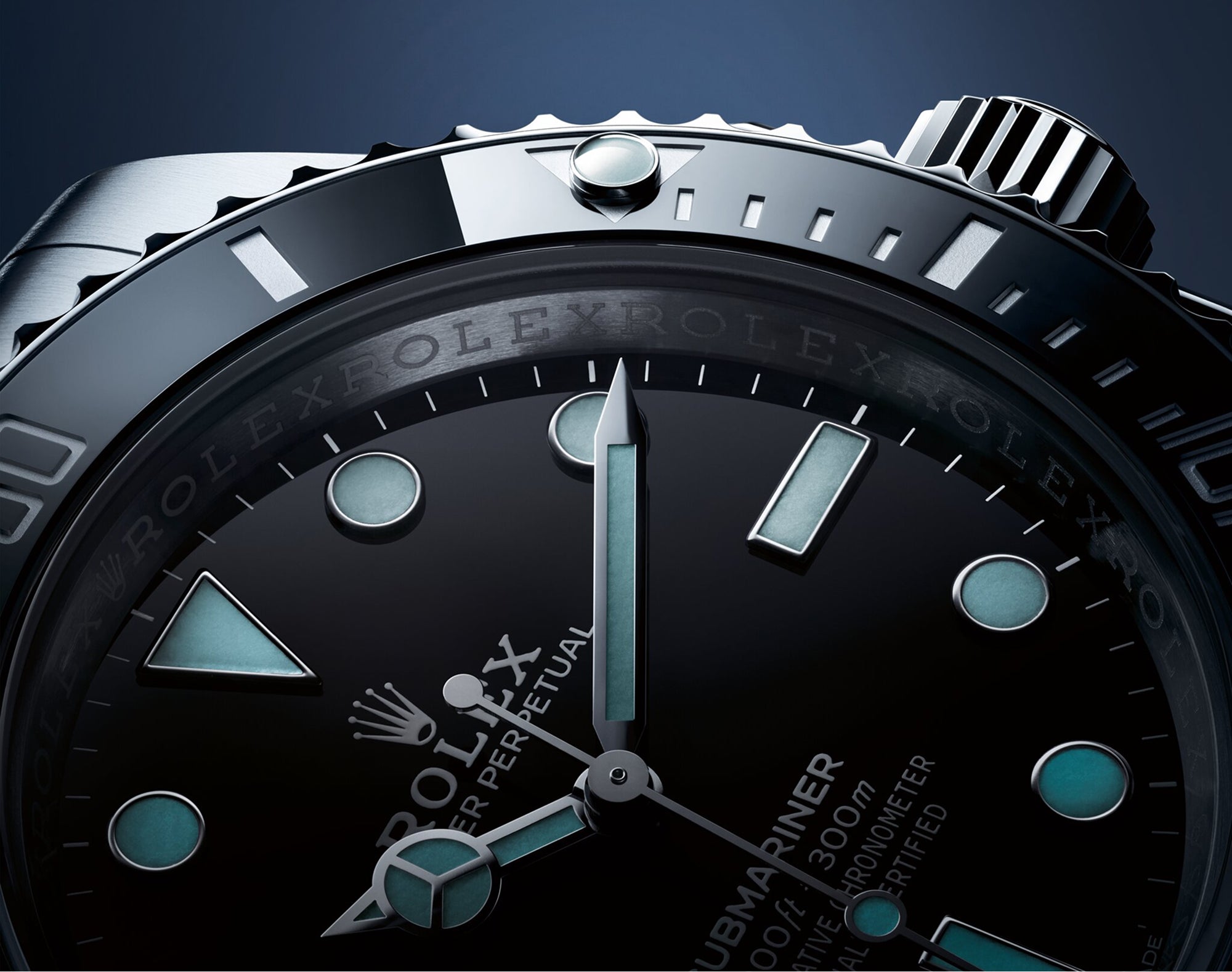 Nahaufnahme des Zifferblatts einer Rolex Submariner, die das schwarze Zifferblatt, die leuchtenden Indizes und Zeiger, den Lünettenrand sowie detaillierte Gravuren zeigt, die vor dem dunklen Hintergrund alle in blauem Licht erstrahlen.
