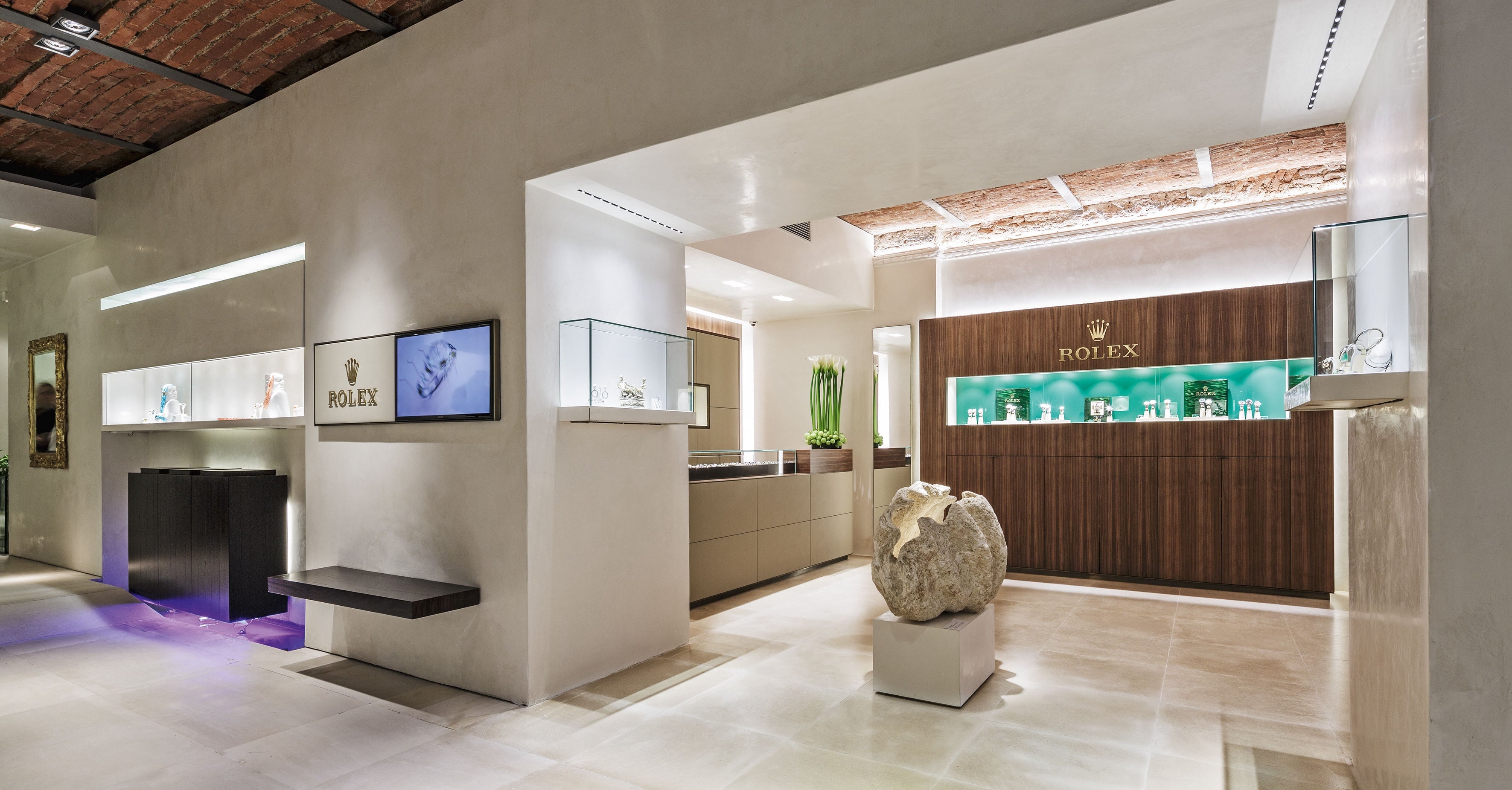 Ein luxuriöser Rolex-Laden mit elegantem, modernem Design. Vitrinen präsentieren verschiedene Uhren, wobei das zentrale Exponat auf einem Podest steht. Sanfte Beleuchtung hebt das elegante Dekor und die Ziegeldeckenakzente hervor.