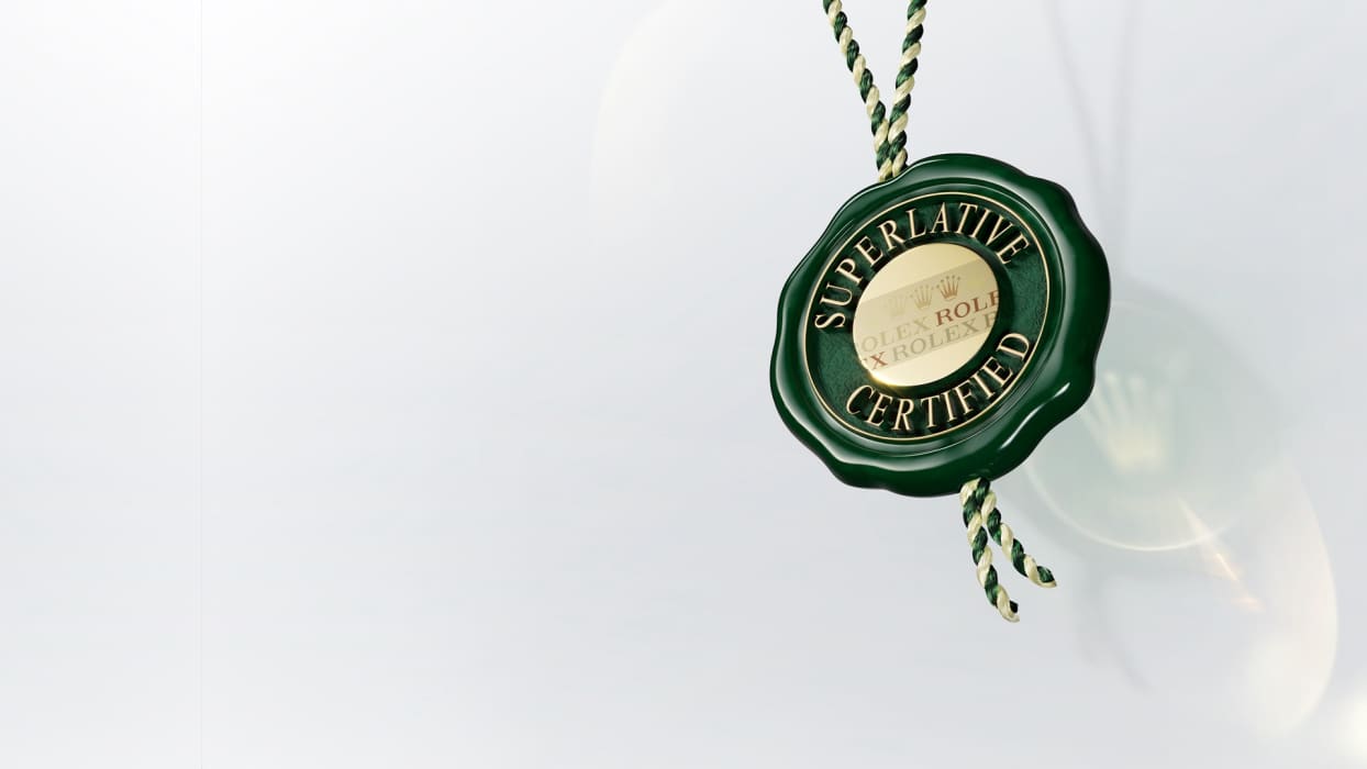 Ein grünes Etikett mit goldenem Text, auf dem „Superlative“ und „Certified“ stehen, und im Hintergrund das teilweise verdeckte Wort „Rolex“. Das Etikett ist an einer grün-goldenen geflochtenen Schnur auf einer weißen Oberfläche befestigt.
