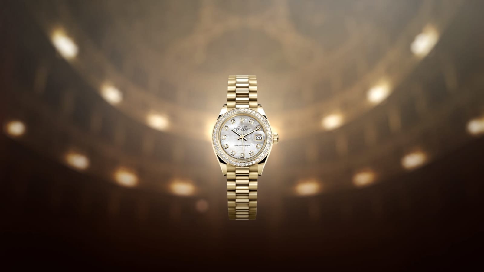 Eine goldene Armbanduhr mit diamantbesetzter Lünette steht zentriert vor einem verschwommenen, warm beleuchteten Hintergrund. Die Uhr hat ein weißes Zifferblatt mit goldenen Stundenmarkierungen und einer Datumsanzeige. Das Armband hat ein klassisches Gliederdesign.