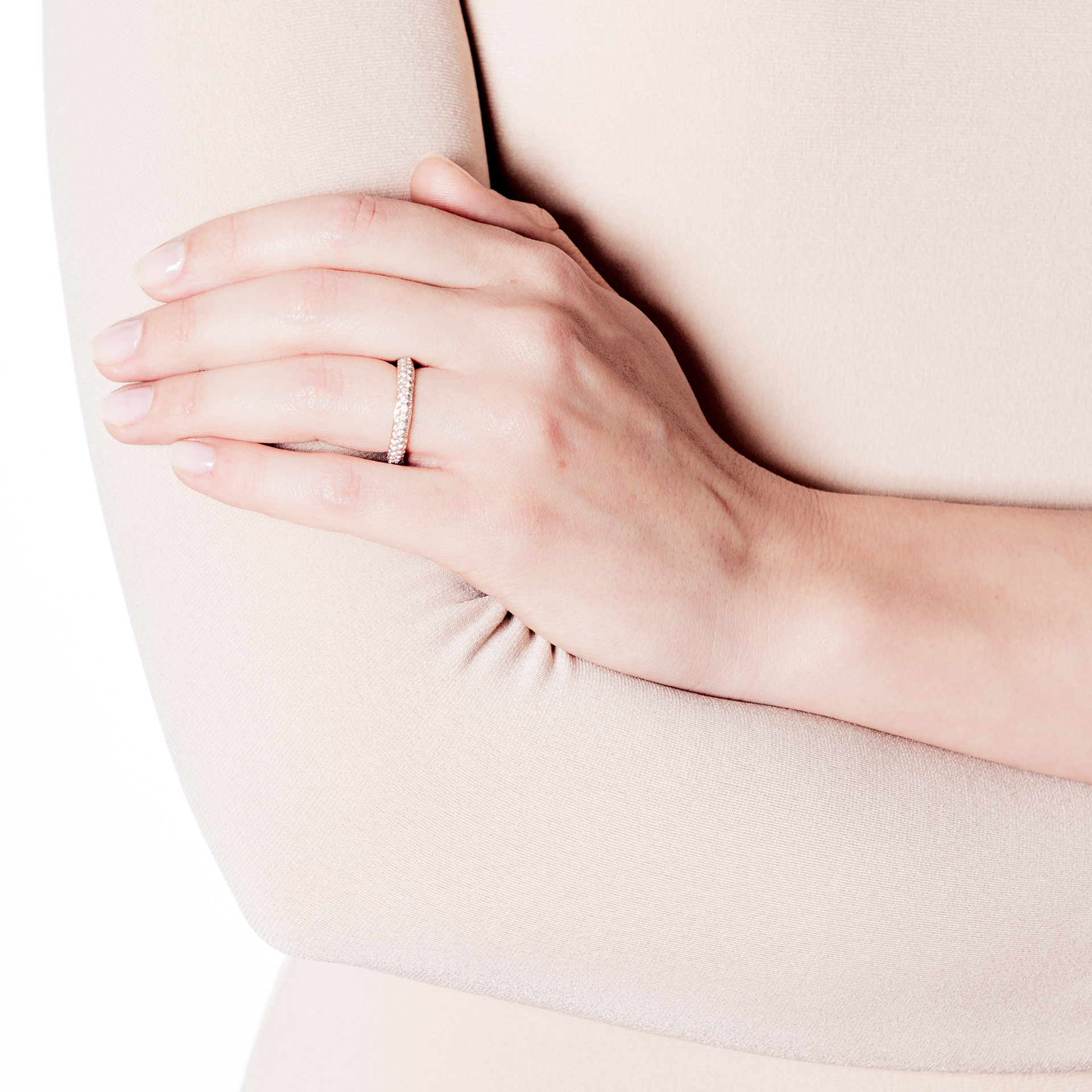 Eine Nahaufnahme einer Person, die ein beiges Langarmshirt trägt und die Arme vor der Brust verschränkt. Eine Hand ruht auf dem Arm, geschmückt mit einem funkelnden MEMOIRE RING von Schullin in Roségold, besetzt mit kleinen Diamanten. Der Hintergrund ist schlicht weiß.