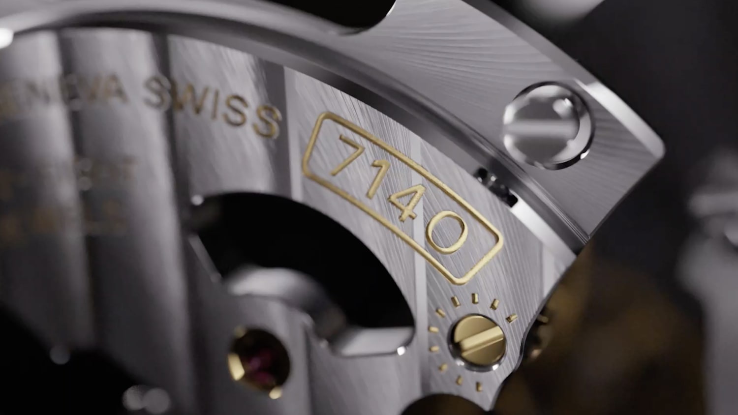 Nahaufnahme eines Luxusuhrwerks mit aufwendigen Details und Gravuren. Die Nummer „7140“ ist in Gold auf einer polierten, metallischen Oberfläche deutlich zu erkennen. Daneben sind auch die Worte „GENEVA SWISS“ eingraviert.