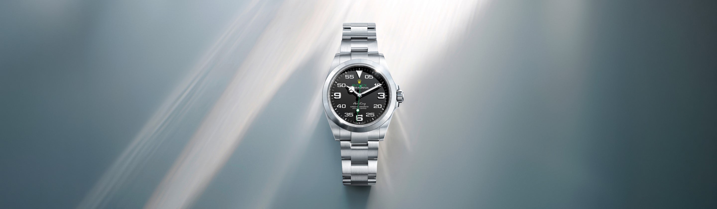 Eine silberne Armbanduhr mit schwarzem Zifferblatt und silbernem Armband ist auf einem weichen, verschwommenen grauen Hintergrund mit Lichtstreifen zentriert.