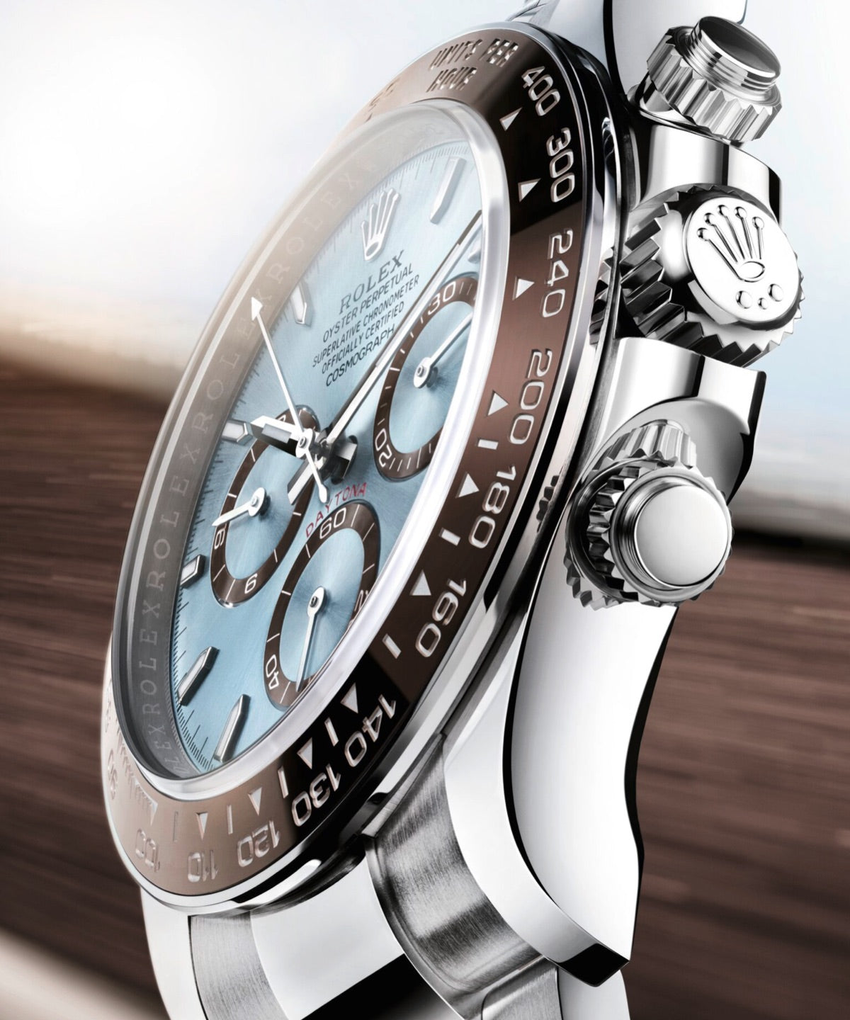 Nahaufnahme einer Luxusuhr in Silber und Blau. Das Zifferblatt zeigt Chronographenzifferblätter und ist von einer Metalllünette mit eingravierten Zahlen umgeben. Die Krone zeigt ein Logo und der Hintergrund ist abstrakt und verschwommen.