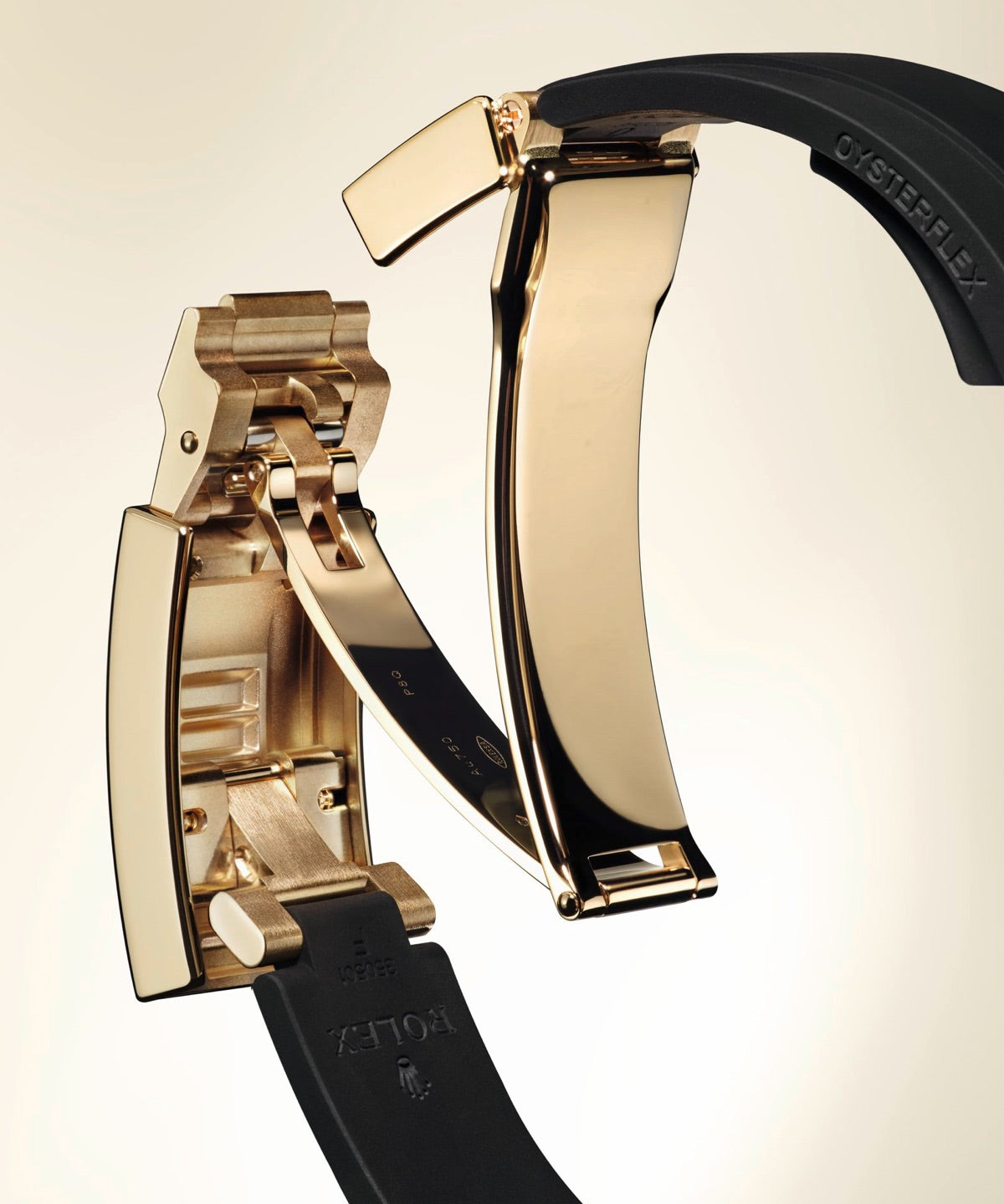 Nahaufnahme einer luxuriösen Armbanduhrschließe mit polierten Goldkomponenten und einem schwarzen Gummiarmband mit sichtbaren eingravierten Markennamen.