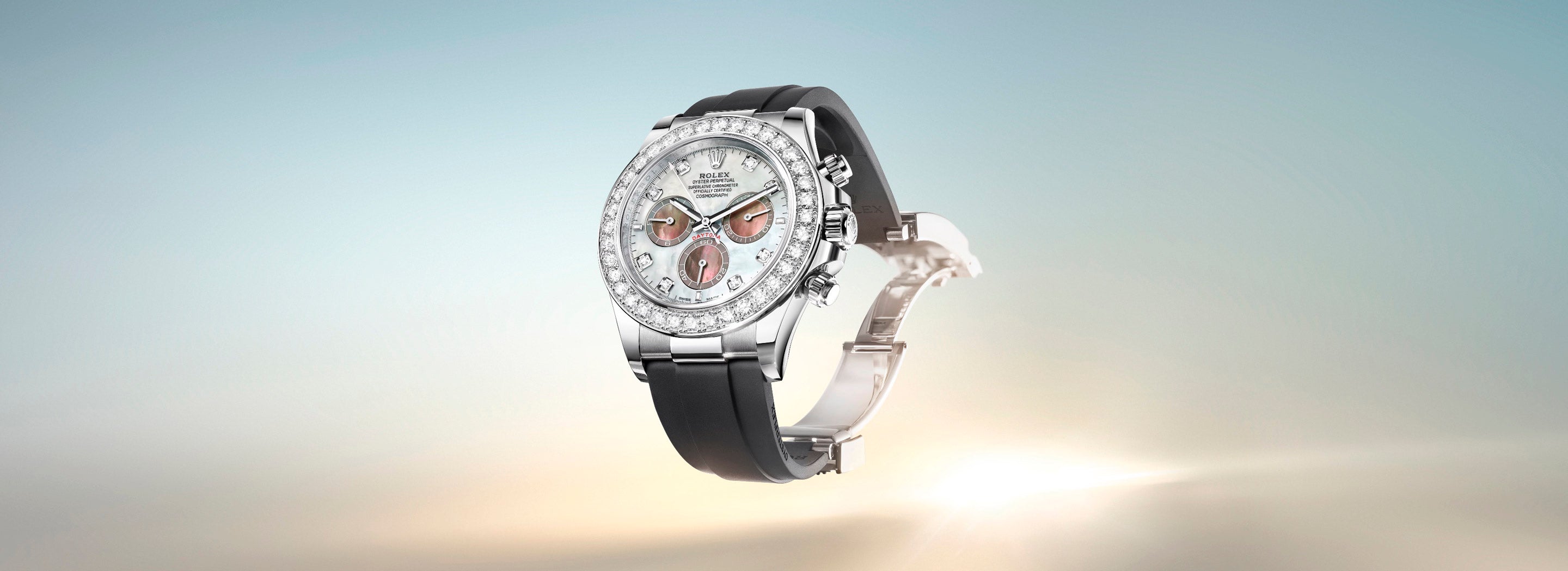 Luxuriöse Armbanduhr mit silbernem Gehäuse, edelsteinbesetzter Lünette und dunklem Armband vor einem Hintergrund mit sanftem Farbverlauf. Das Zifferblatt verfügt über drei Hilfszifferblätter mit roten Akzenten.