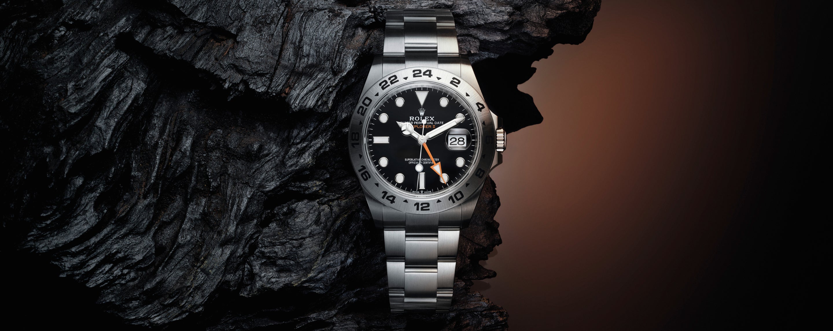 Eine silberne Rolex-Uhr mit schwarzem Zifferblatt und weißen Stundenmarkierungen steht aufrecht vor einem dunklen, strukturierten Hintergrund, der an Baumrinde erinnert, mit warmer Beleuchtung auf der rechten Seite.