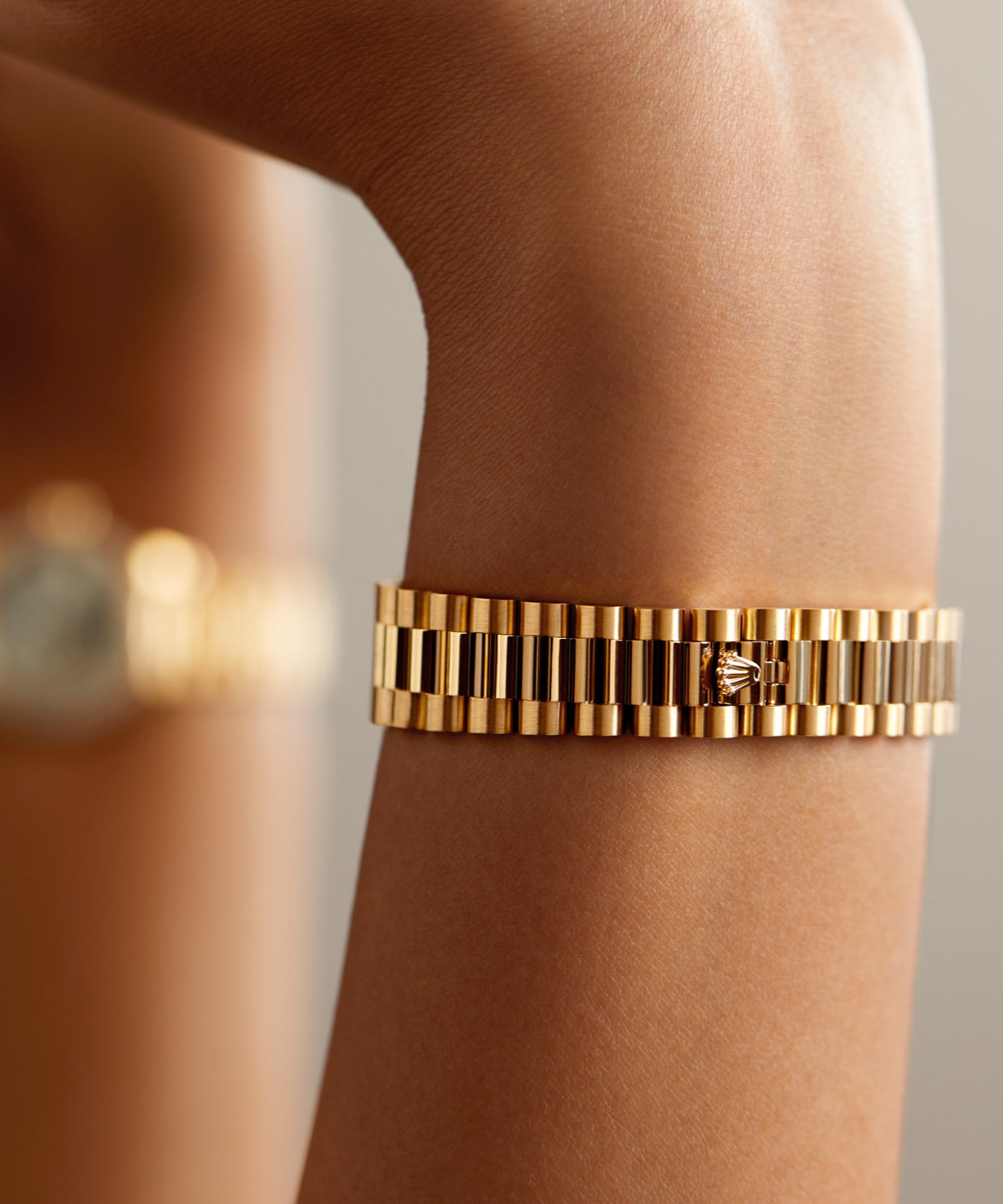 Nahaufnahme eines goldenen Armbands am Handgelenk einer Person mit einem gemusterten Design mit abwechselnd polierten und matten Gliedern. Das Armband reflektiert Licht und hebt seine glänzende Textur vor einem unscharfen Hintergrund hervor.