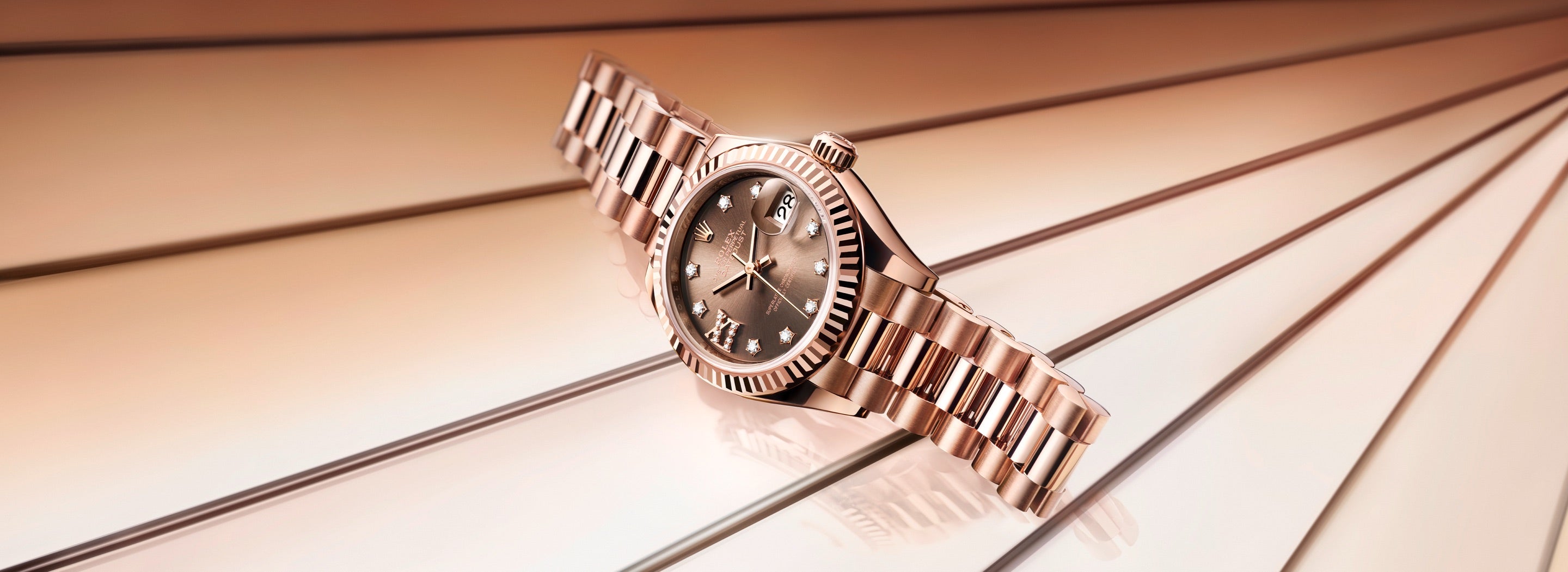 Eine luxuriöse Armbanduhr aus Roségold mit Metallarmband wird elegant auf einer reflektierenden Oberfläche präsentiert. Das Zifferblatt hat Diamant-Stundenmarkierungen und der Hintergrund weist subtile, parallele Linien in warmen Tönen auf.