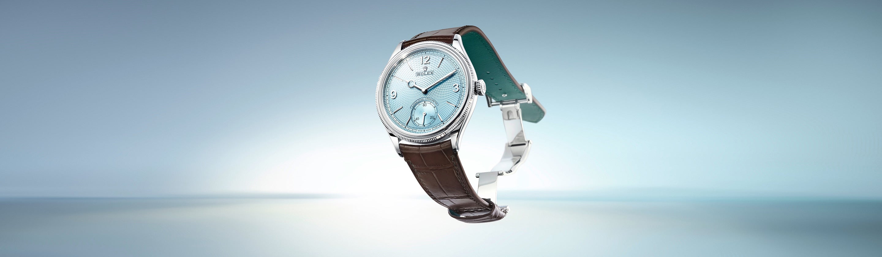 Eine luxuriöse Armbanduhr mit einem hellblauen, strukturierten Zifferblatt mit silbernen Stunden- und Minutenzeigern und einem kleinen Sekunden-Hilfszifferblatt. Sie hat ein braunes Lederarmband mit einer silbernen Schnalle vor einem verschwommenen hellblauen Hintergrund.