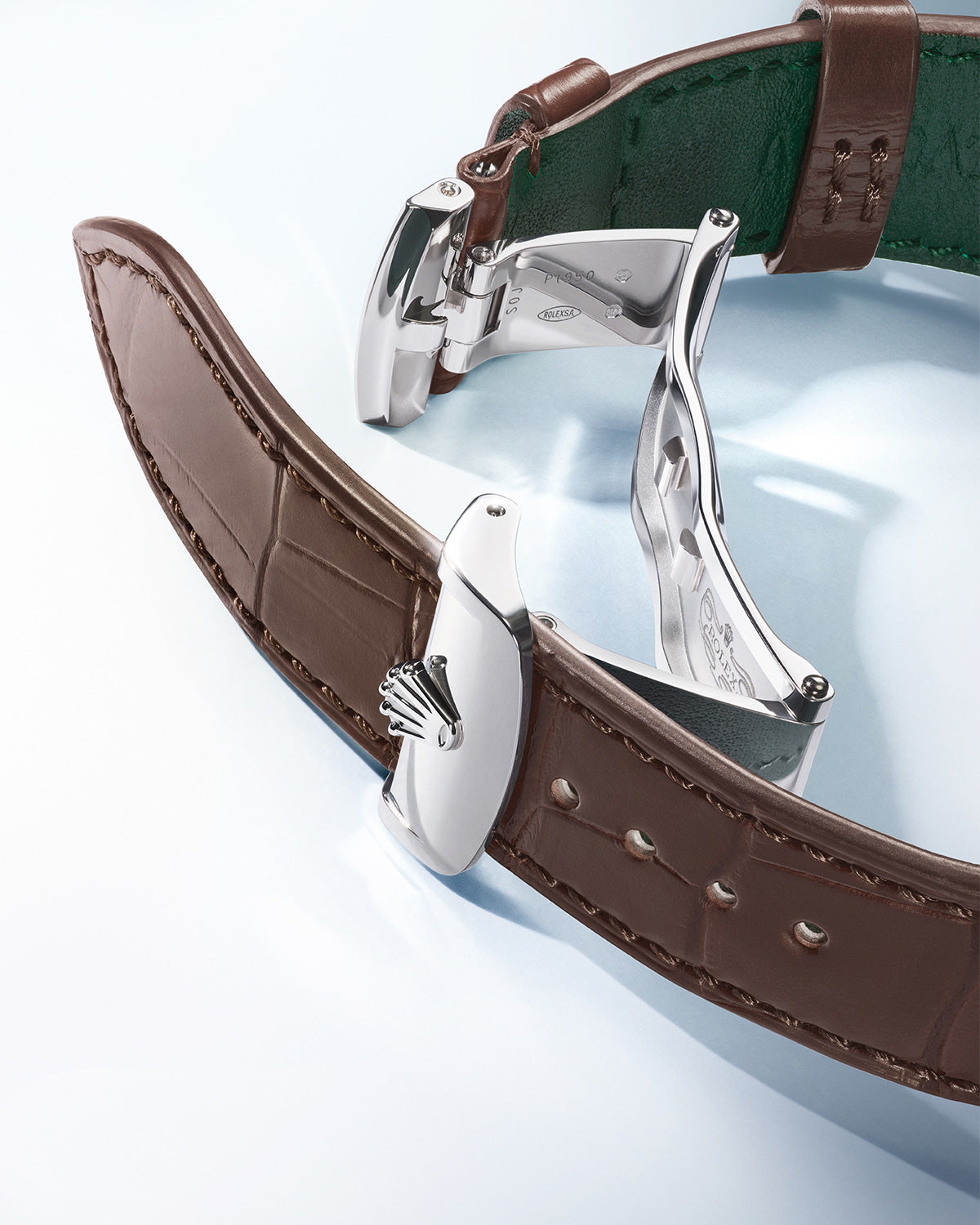 Nahaufnahme einer Uhr mit einem braunen Lederarmband und einem silbernen Verschluss. Der Verschluss ist geöffnet und zeigt seinen metallischen Glanz. Darauf ist ein Logo eingeprägt. Das Armband ist strukturiert und das Innenfutter ist grün. Der Hintergrund ist sanft beleuchtet.