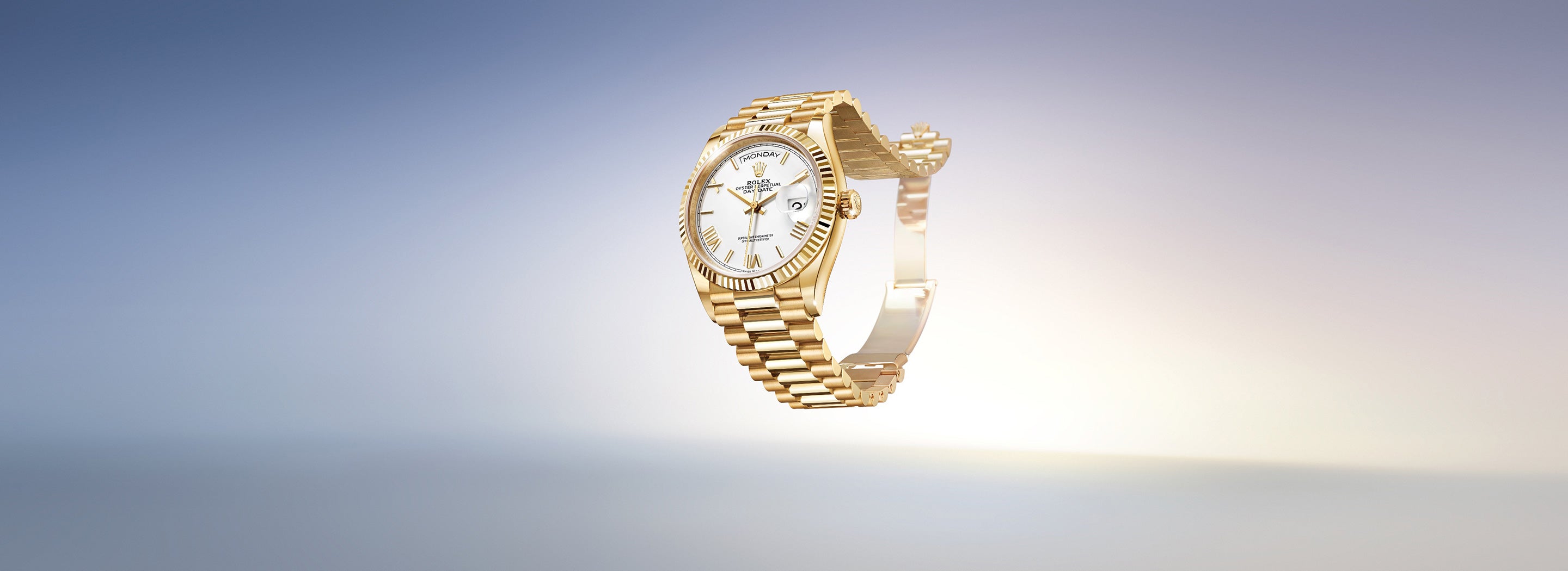 Eine goldene Armbanduhr mit geriffelter Lünette und weißem Zifferblatt schwebt vor einem Farbverlaufshintergrund, der von Blau nach Beige übergeht. Die Uhr hat ein Gliederarmband und ein Datumsanzeigefenster.