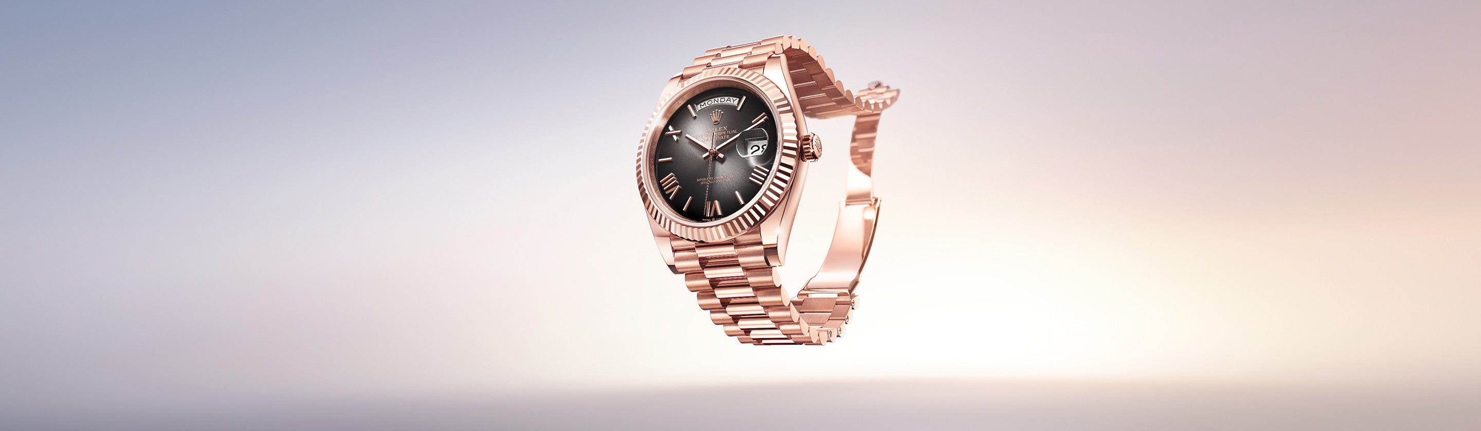 Eine Armbanduhr aus Roségold mit schwarzem Zifferblatt und römischen Stundenmarkierungen vor einem Hintergrund mit Farbverlauf in sanften Pastelltönen. Die Uhr verfügt über eine geriffelte Lünette und ein Metallarmband mit Gliedern.