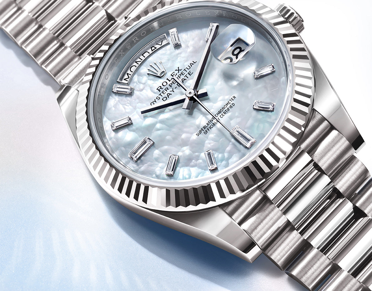 Eine Luxusuhr mit silbernem Metallarmband und strukturiertem weißen Zifferblatt. Die Uhr verfügt über eine Tages- und Datumsanzeige mit auffälligen Stundenmarkierungen und eingraviertem Text auf der Lünette. Das aufwendig gestaltete Armband reflektiert Licht.