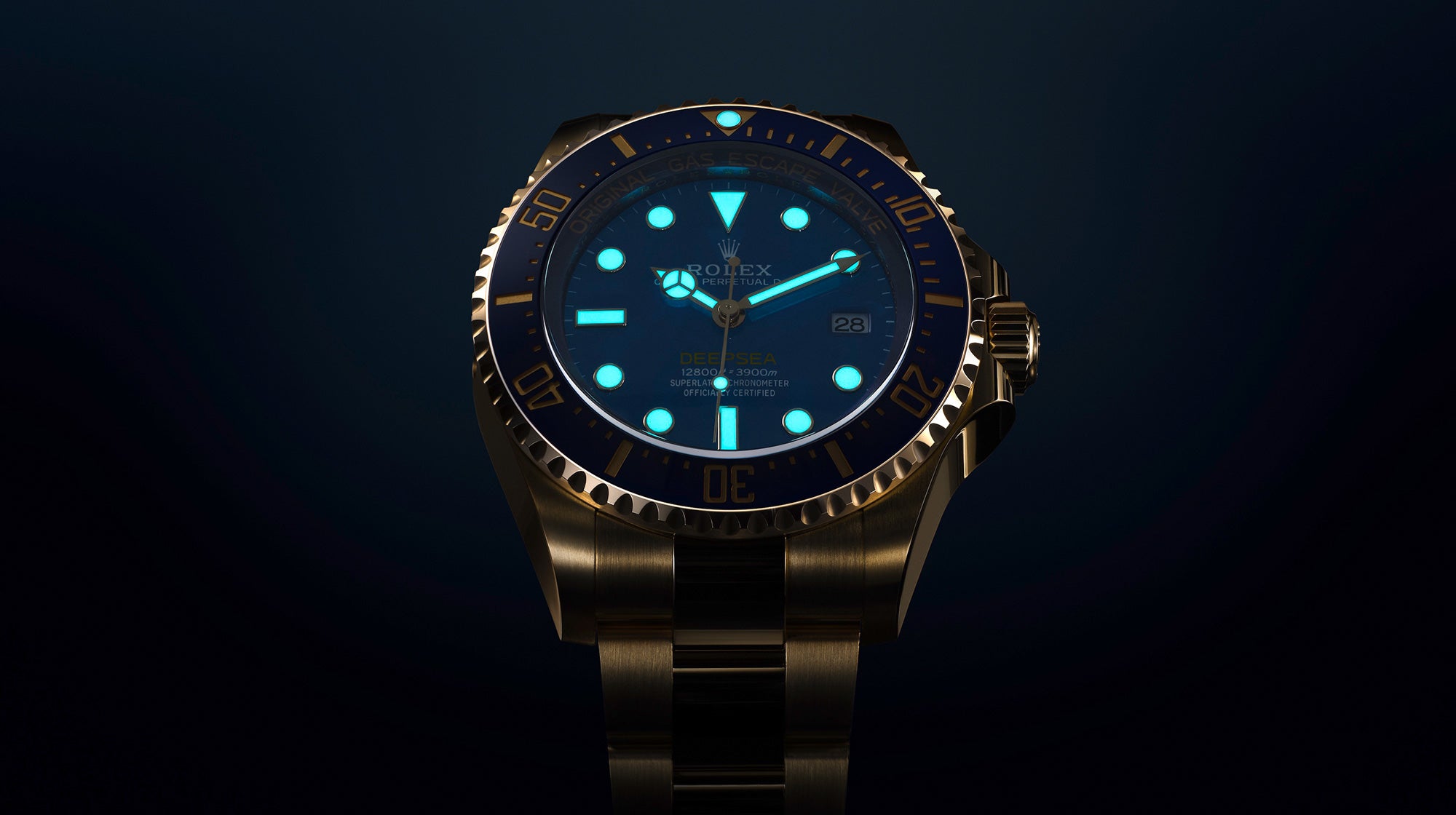 Abgebildet ist eine leuchtende Armbanduhr mit einem goldfarbenen Metallarmband und einem dunkelblauen Zifferblatt. Das Zifferblatt hat leuchtende Stundenmarkierungen und Zeiger, mit einer Datumsanzeige auf der rechten Seite. Die Uhr ist vor einem dunklen Hintergrund angebracht, wodurch ihr kompliziertes Design hervorgehoben wird.