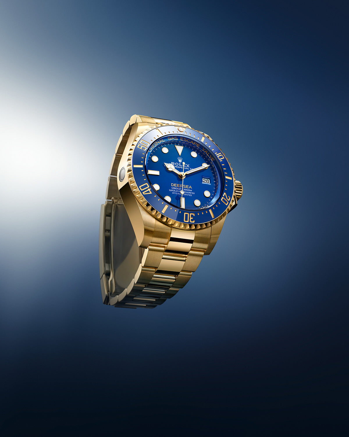Eine luxuriöse goldene Armbanduhr mit blauem Zifferblatt und Lünette ist vor einem Hintergrund mit Farbverlauf in Blau zu sehen. Die Uhr zeigt die Zeit mit leuchtenden Zeigern und Markierungen an.