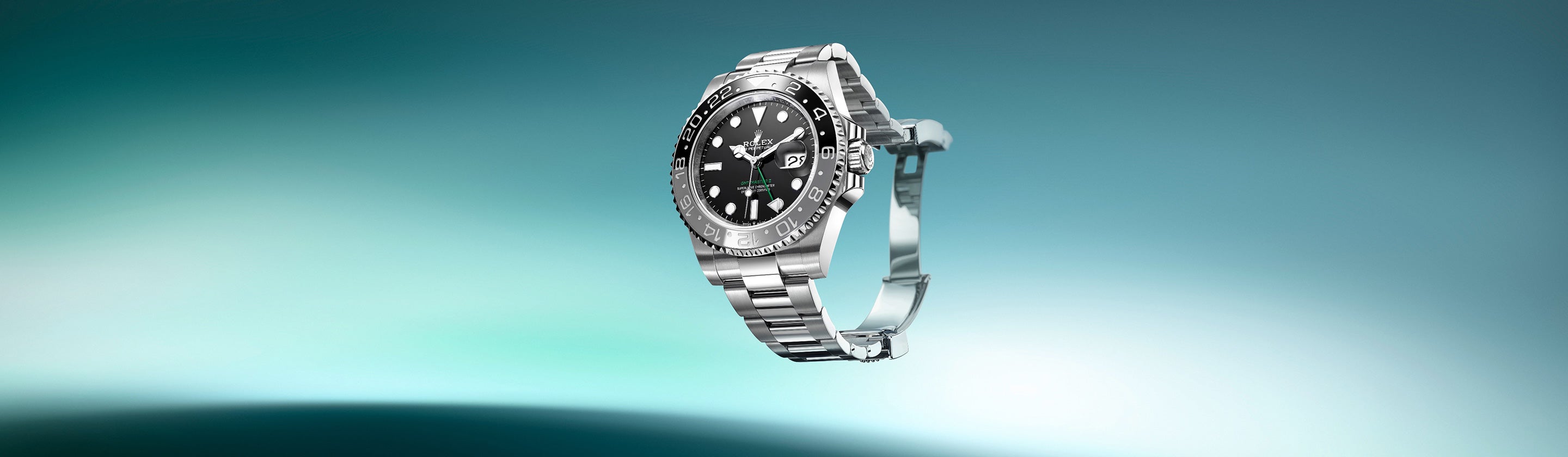 Silberne Armbanduhr mit schwarzem Zifferblatt und Datumsanzeige vor einem verschwommenen grün-weißen Farbverlaufshintergrund. Die Uhr verfügt über ein Metallgliederarmband und eine drehbare Lünette.