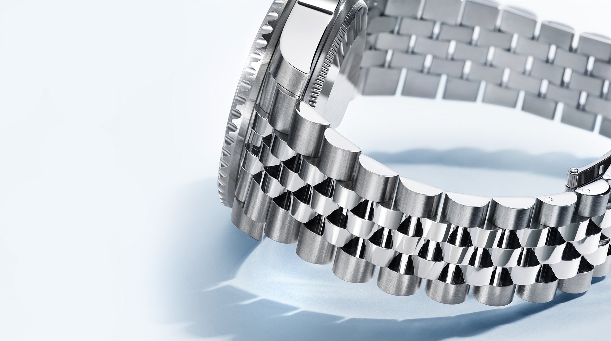 Nahaufnahme einer Luxusuhr mit poliertem Metallarmband, das sein kompliziertes Gliederdesign zur Schau stellt. Die Uhr ist teilweise sichtbar, was die Handwerkskunst des Armbands vor einem weichen, hellen Hintergrund hervorhebt.