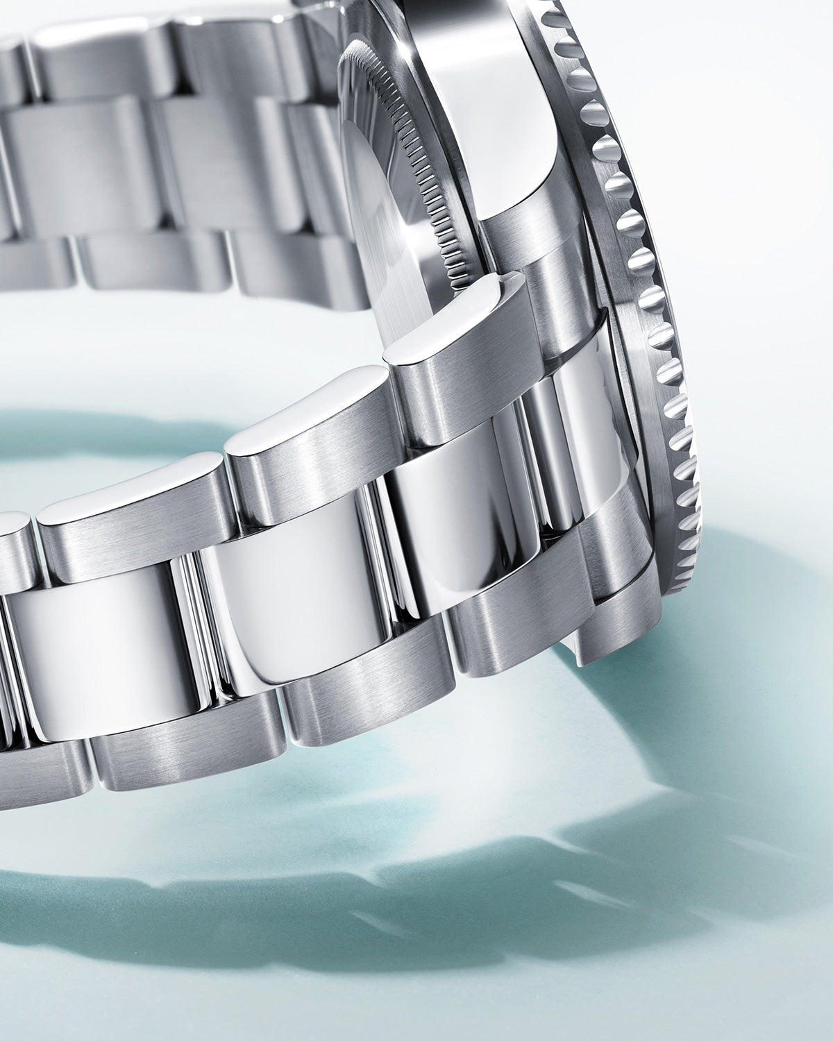 Nahaufnahme eines Edelstahlarmbands auf hellem Hintergrund. Das Armband besteht aus polierten und gebürsteten Metallgliedern, die seine glatte und reflektierende Oberfläche zur Schau stellen. Der Rand der Uhr ist auf der rechten Seite des Bildes leicht sichtbar.