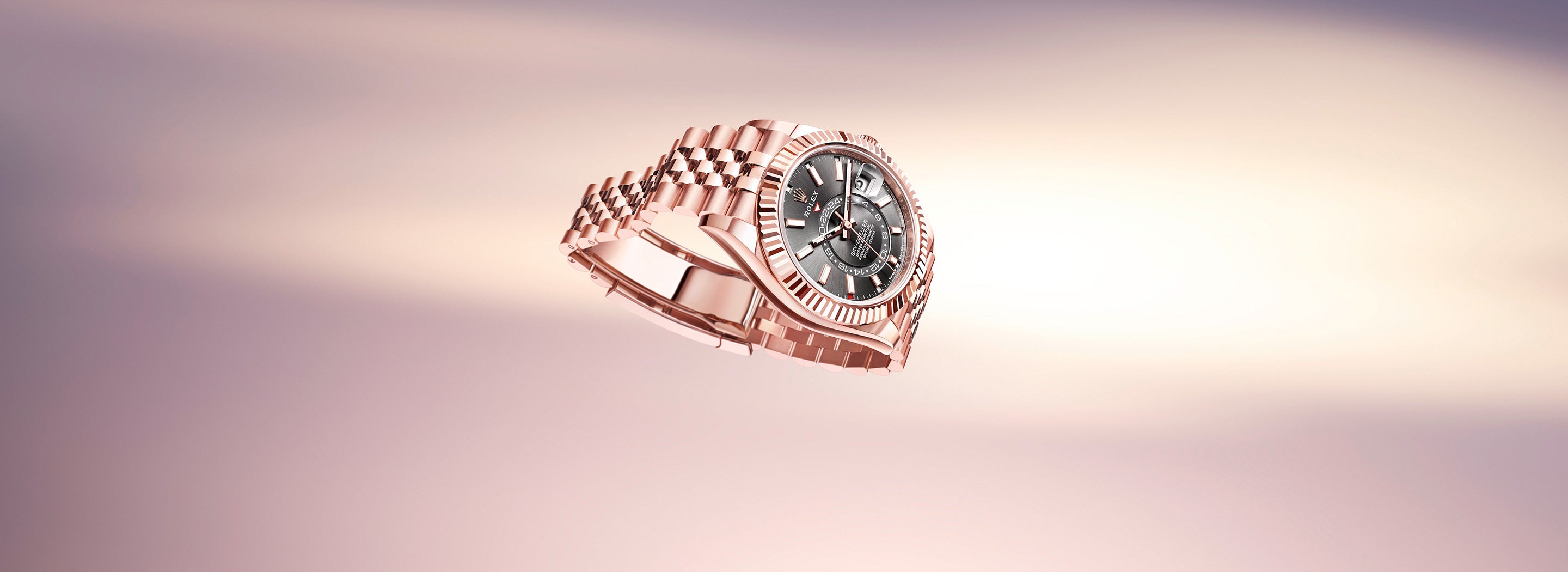 Eine Armbanduhr aus Roségold mit detailliertem Zifferblatt und Metallarmband schwebt anmutig vor einem weichen, verschwommenen Hintergrund in Rosa und hellen Farbtönen. Das Uhrendesign zeichnet sich durch römische Ziffern und aufwendige Details aus.
