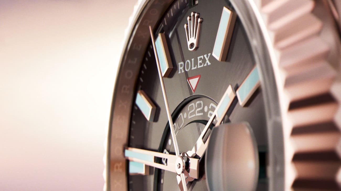 Nahaufnahme eines Rolex-Zifferblatts mit Markenlogo, silbernen Stundenmarkierungen, Zeigern und einer Datumsanzeige. Die Uhr hat eine Metalllünette mit eingraviertem Text und der Hintergrund ist sanft verschwommen, was das elegante Design hervorhebt.