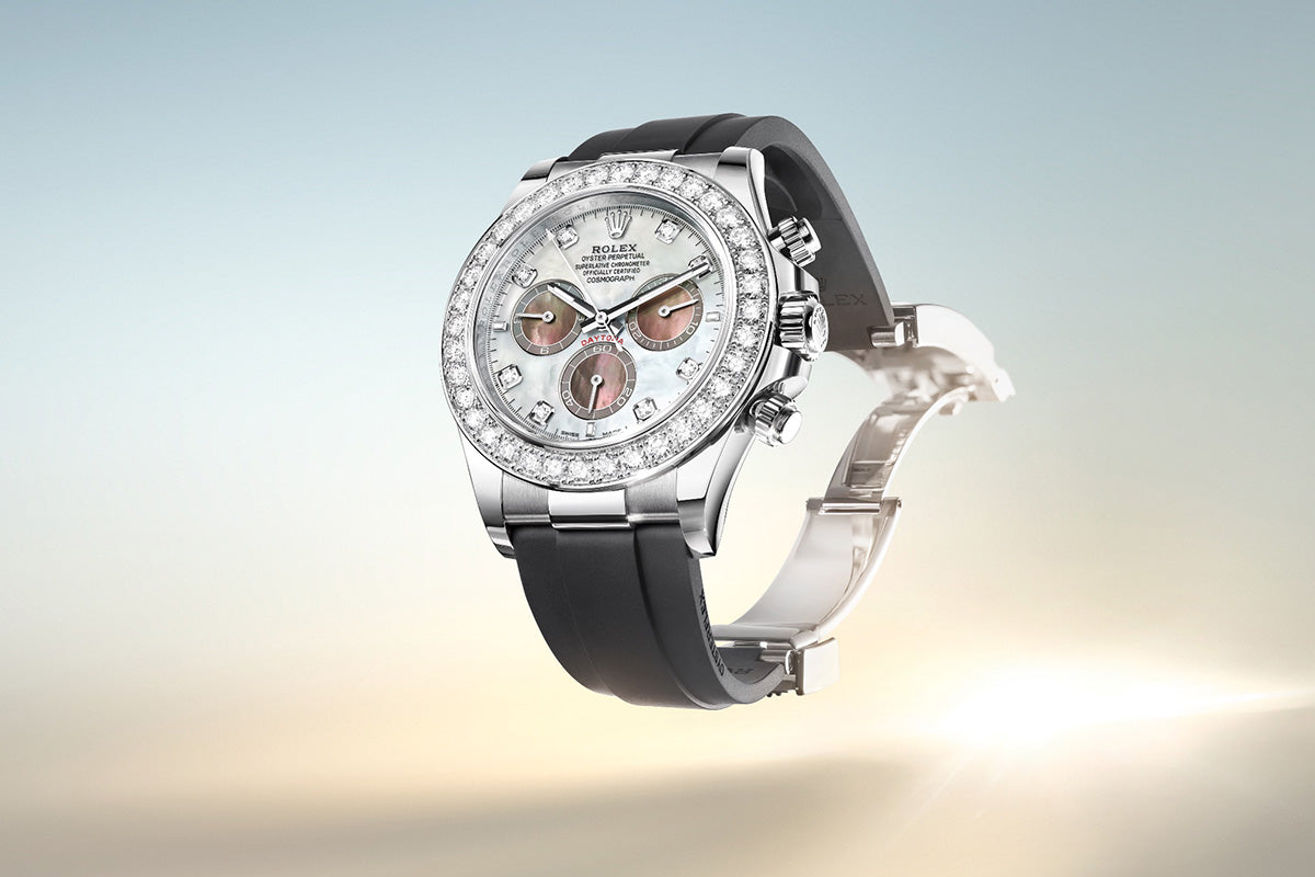 Eine luxuriöse Armbanduhr mit silberner und diamantbesetzter Lünette, weißem Zifferblatt und drei Hilfszifferblättern. Sie hat ein elegantes schwarzes Armband auf einem weichen Hintergrund mit Farbverlauf von Blau nach Beige.