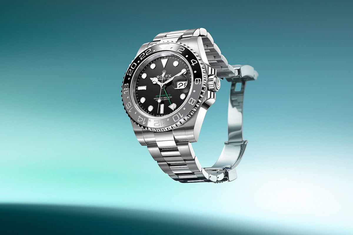 Eine stilvolle silberne Armbanduhr mit schwarzem Zifferblatt vor einem türkisfarbenen Hintergrund mit Farbverlauf. Die Uhr verfügt über eine Datumsanzeige und ein silbernes Metallarmband. Das Licht wird von der polierten Oberfläche reflektiert und unterstreicht das elegante Design.