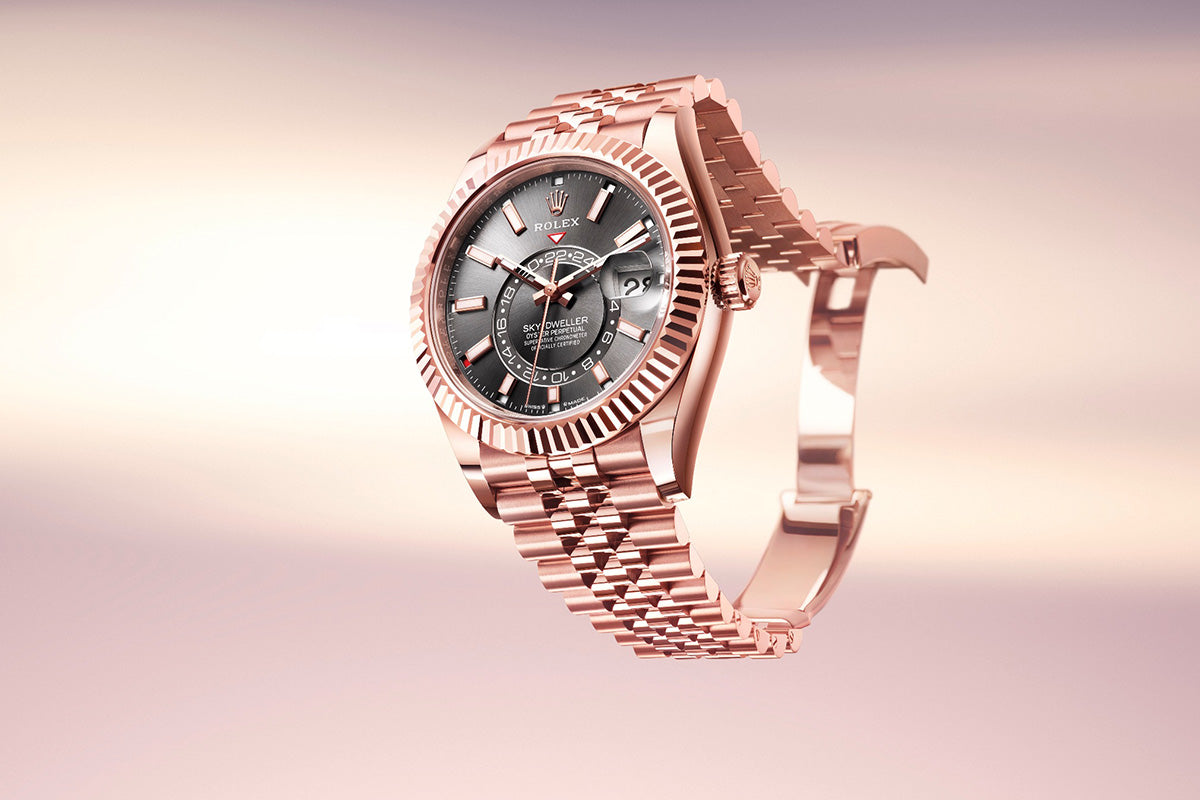 Eine luxuriöse Armbanduhr aus Roségold mit einem metallisch grauen Zifferblatt, einer Datumsanzeige und römischen Stundenmarkierungen. Die Uhr ist vor einem sanften rosa-beigen Farbverlaufshintergrund angebracht, der ihr elegantes Design hervorhebt.
