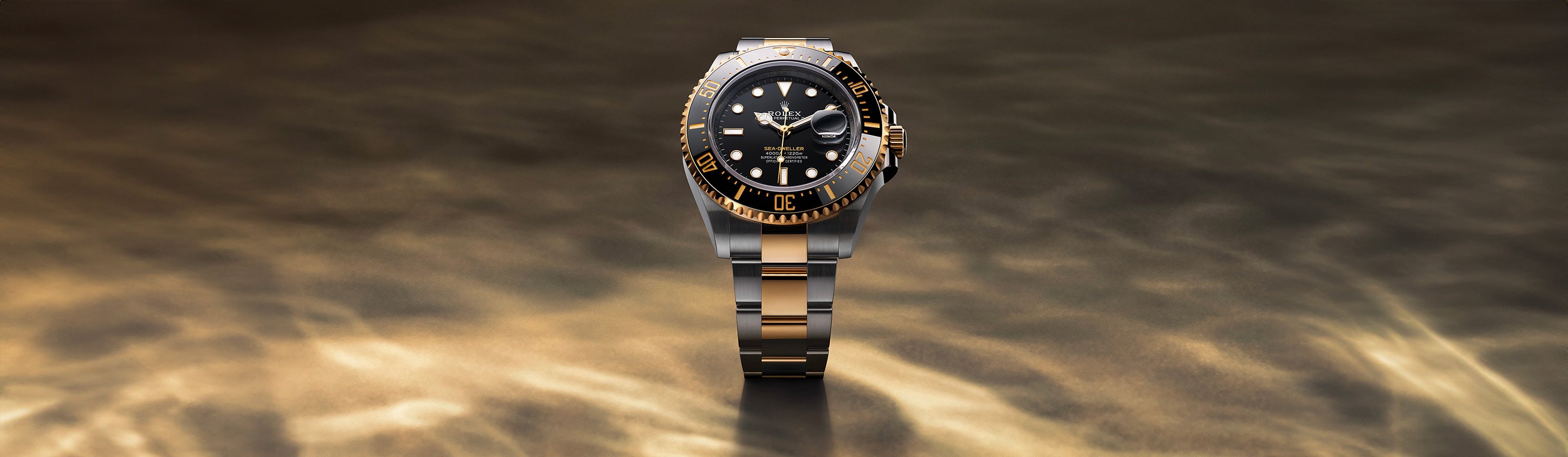 Eine Luxusuhr mit schwarz-goldenem Design wird elegant vor einem weichen, strukturierten braunen Hintergrund präsentiert. Die Uhr verfügt über ein rundes Zifferblatt mit goldenen Akzenten und ein zweifarbiges Metallarmband.