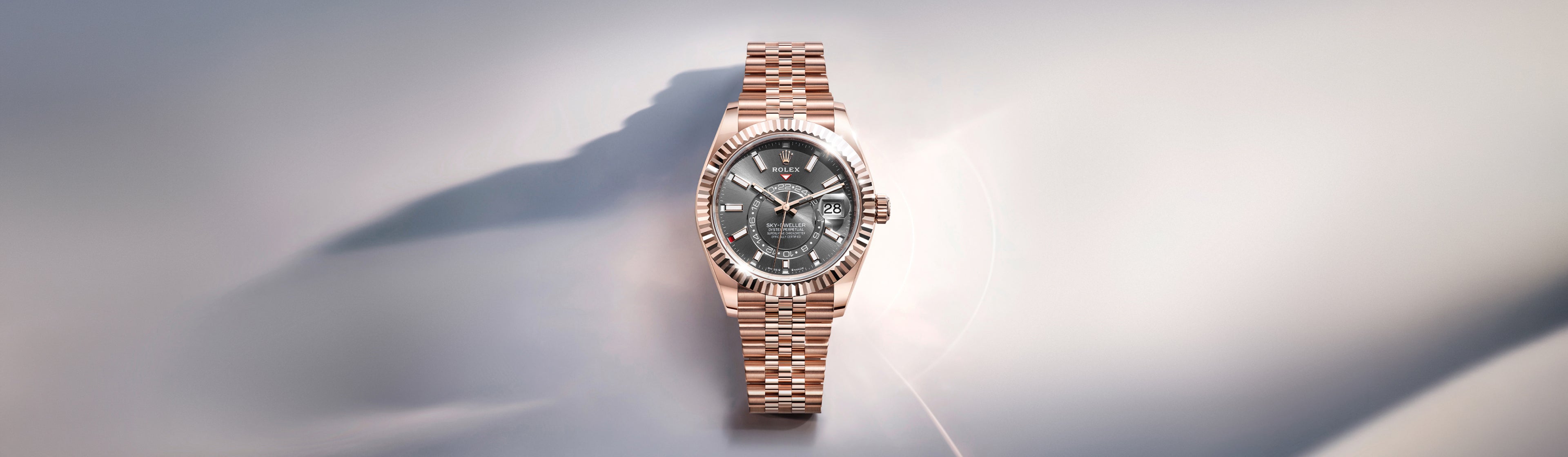 Eine roségoldene Armbanduhr mit geriffelter Lünette und Metallgliederarmband wird auf einem weichen, hellen Hintergrund präsentiert, der ihr elegantes Design und ihr detailliertes Zifferblatt hervorhebt.