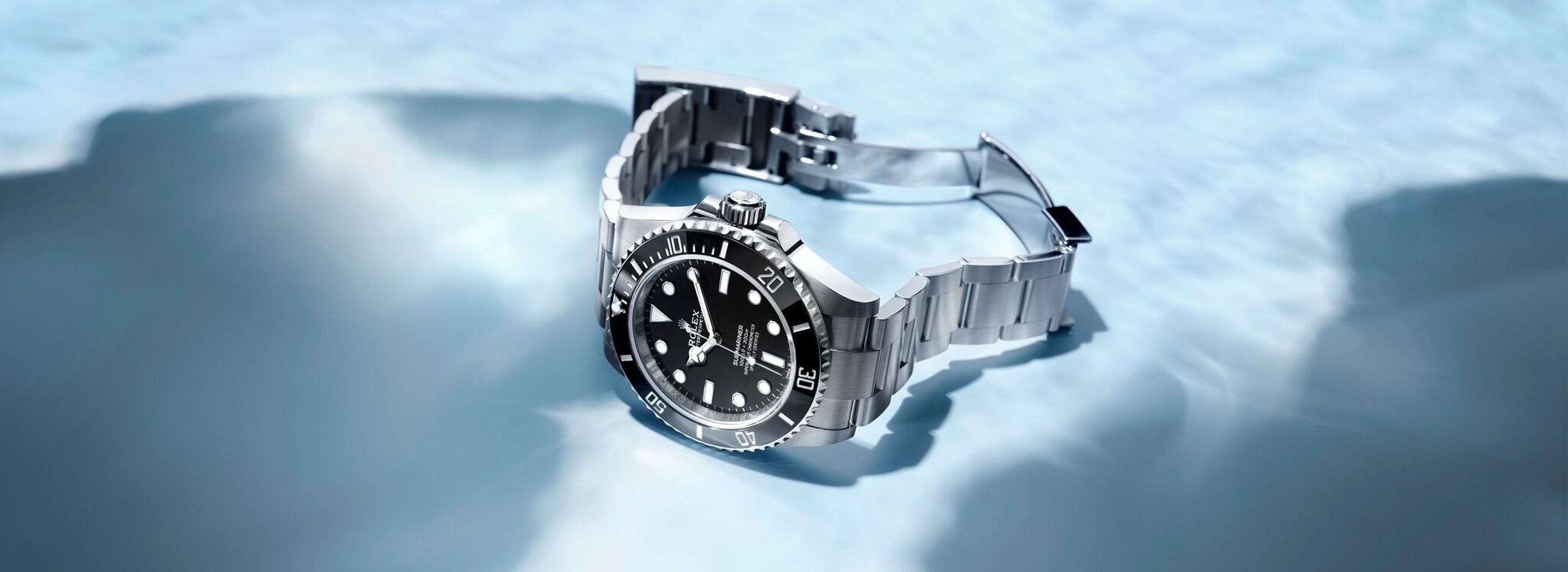 Eine Luxusarmbanduhr aus Edelstahl mit schwarzem Zifferblatt und Lünette ist teilweise in klares, plätscherndes Wasser getaucht, das das Licht reflektiert. Das Uhrenarmband ist offen und die gesamte Szene vermittelt Eleganz und Beständigkeit.