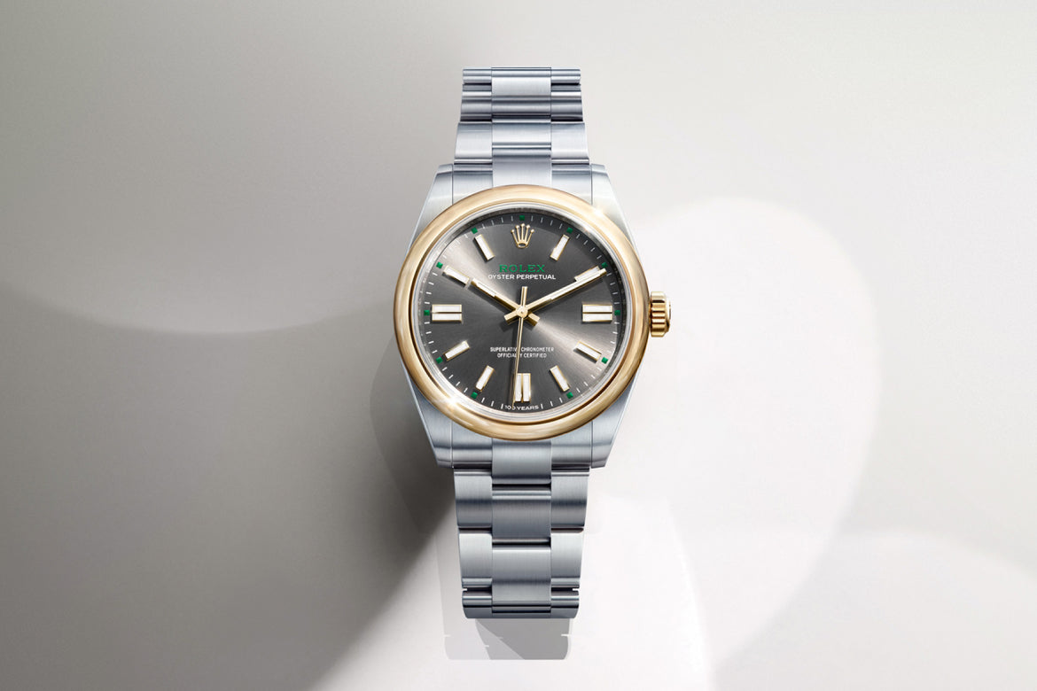 Eine luxuriöse Armbanduhr mit zweifarbigem Metallband, silbernen und goldenen Akzenten und einem dunkelgrauen Zifferblatt mit silbernen Stundenmarkierungen und Zeigern auf einem hellen, sanft strukturierten Hintergrund.