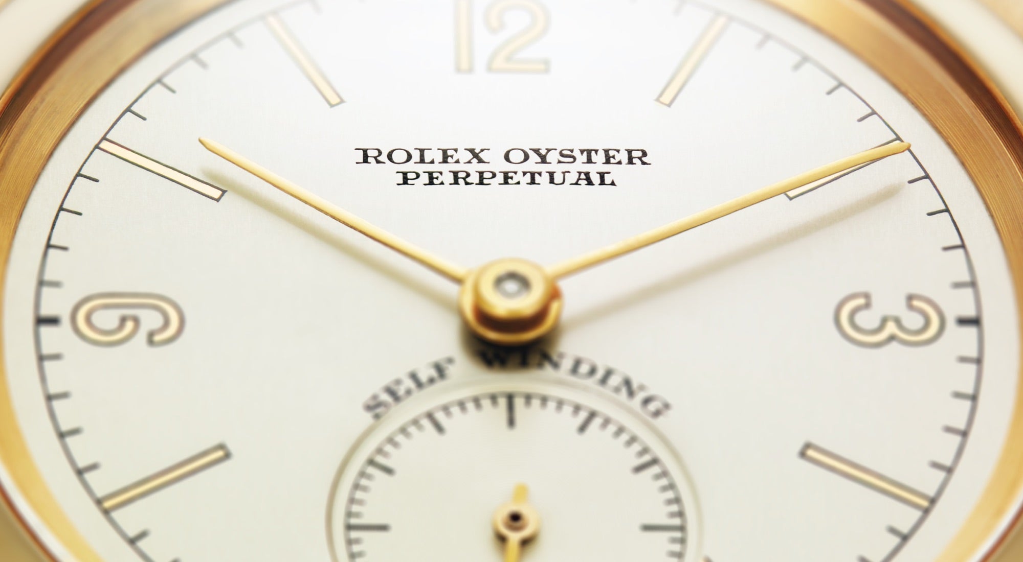 Nahaufnahme eines Zifferblatts einer Rolex Oyster Perpetual mit goldenen Stunden-, Minuten- und Sekundenzeigern. Das Zifferblatt enthält schmale goldene Stundenmarkierungen und zeigt den Text „Rolex Oyster Perpetual“ und „Self Winding“.