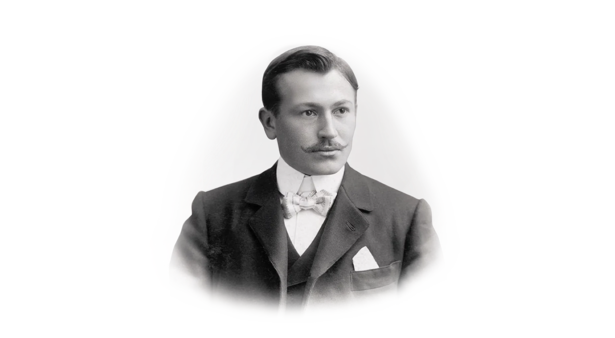 Ein Schwarzweißporträt eines Mannes mit Schnurrbart, der Anzug, Weste, Fliege und Einstecktuch trägt. Er hat ordentlich gekämmtes Haar und blickt leicht nach rechts. Der Hintergrund ist schlicht.