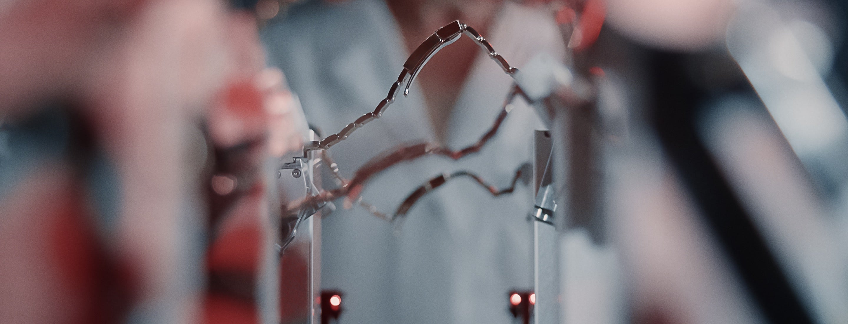 Nahaufnahme komplexer Metallstrukturen, die ein bogenförmiges Muster bilden, mit verschwommenen Elementen im Hintergrund. Das Bild zeigt Reflexionen und Glanzlichter auf dem Metall, während kleine rote Lichter der Szene Kontrast verleihen.