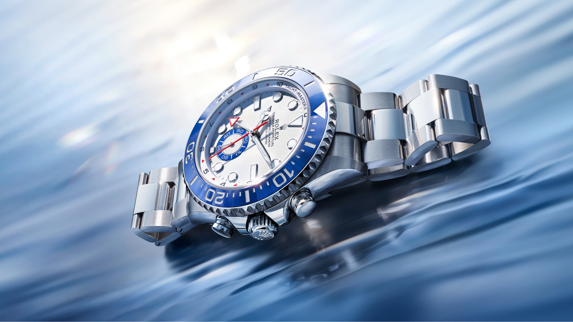 Eine luxuriöse silberne Armbanduhr mit blauer Lünette und weißem Zifferblatt ruht auf einer reflektierenden, kräuselnden Wasseroberfläche, die von sanftem, natürlichem Licht beleuchtet wird.