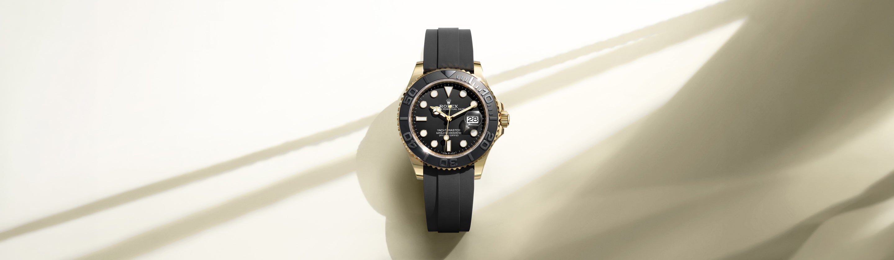 Eine luxuriöse schwarz-goldene Armbanduhr mit schwarzem Kautschukarmband wird auf einer hellen Fläche ausgestellt, wobei weiche Schatten auf den Hintergrund geworfen werden.